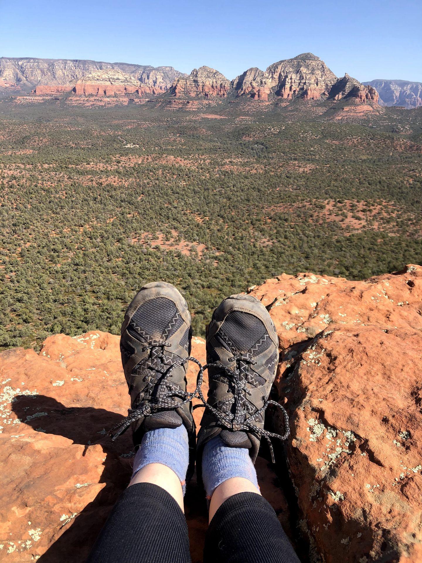 A photo of Lydia's feet wearing Merrell hiking shoes in Sedona. There are red rock mountains far out in the distance.
