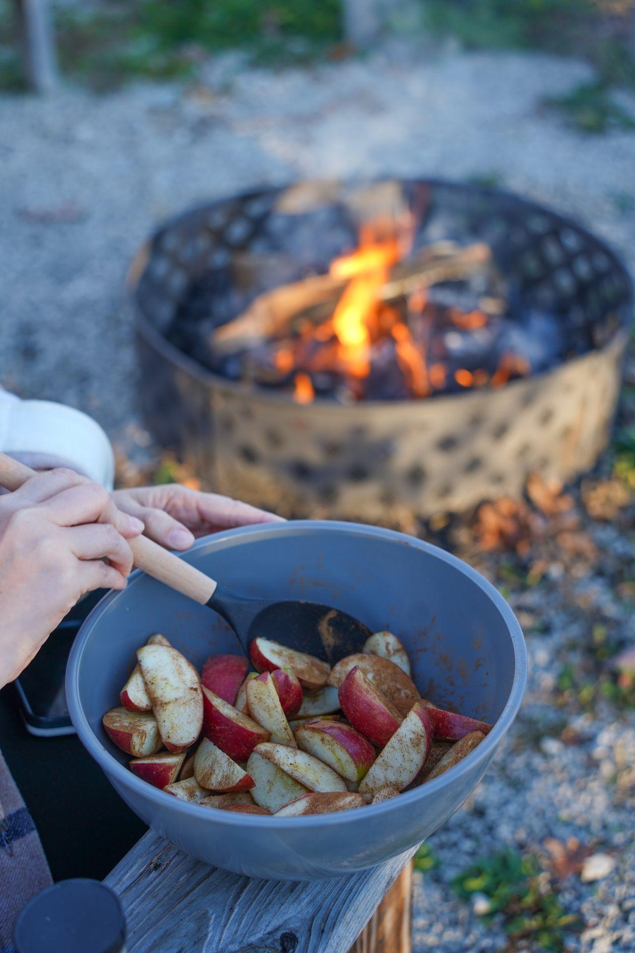 Mixing up apples with sugar in a bowl next to a campfire.