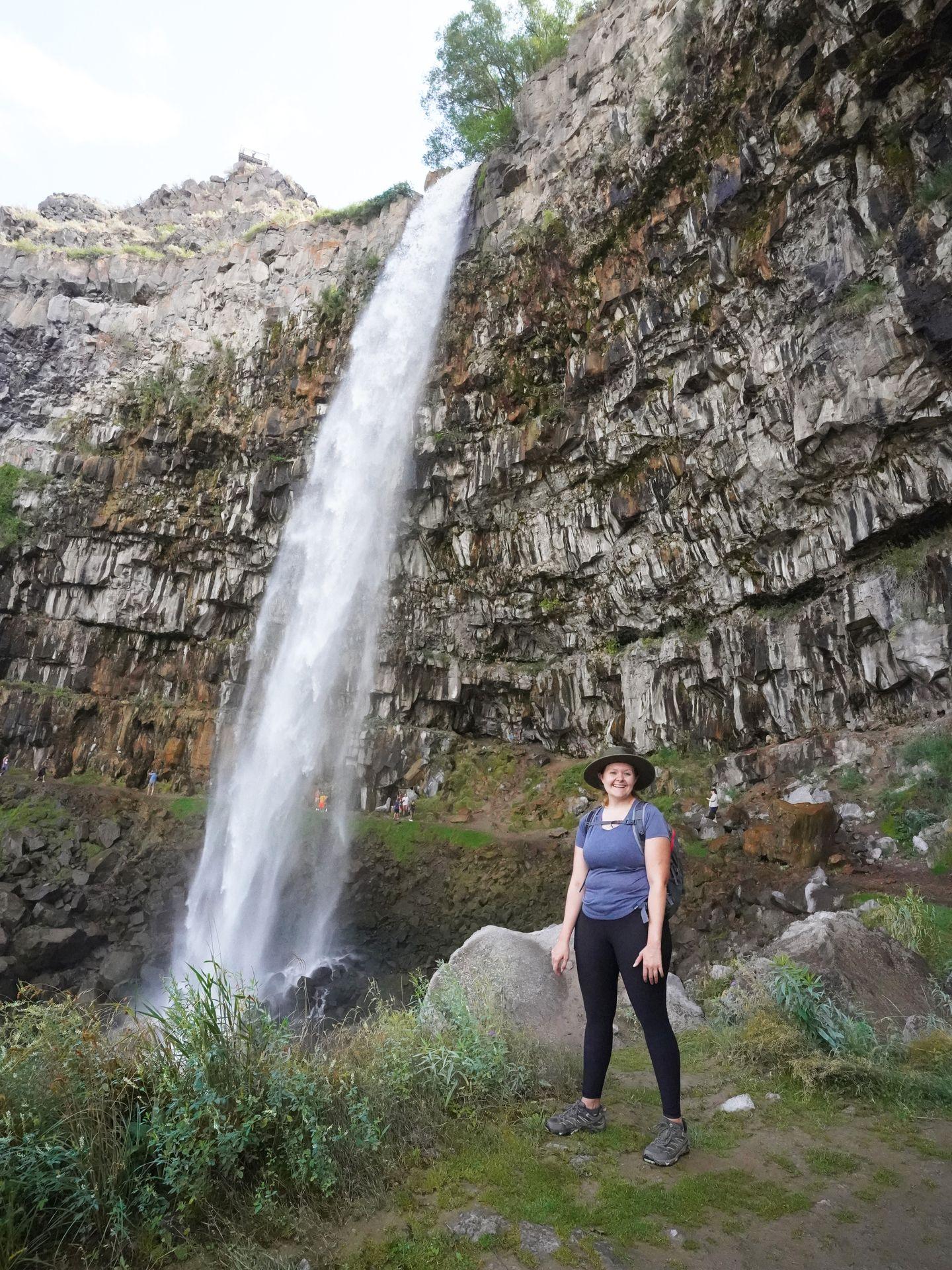Lydia standing in front of a waterfall and wearing a blue Patagonia shirt
