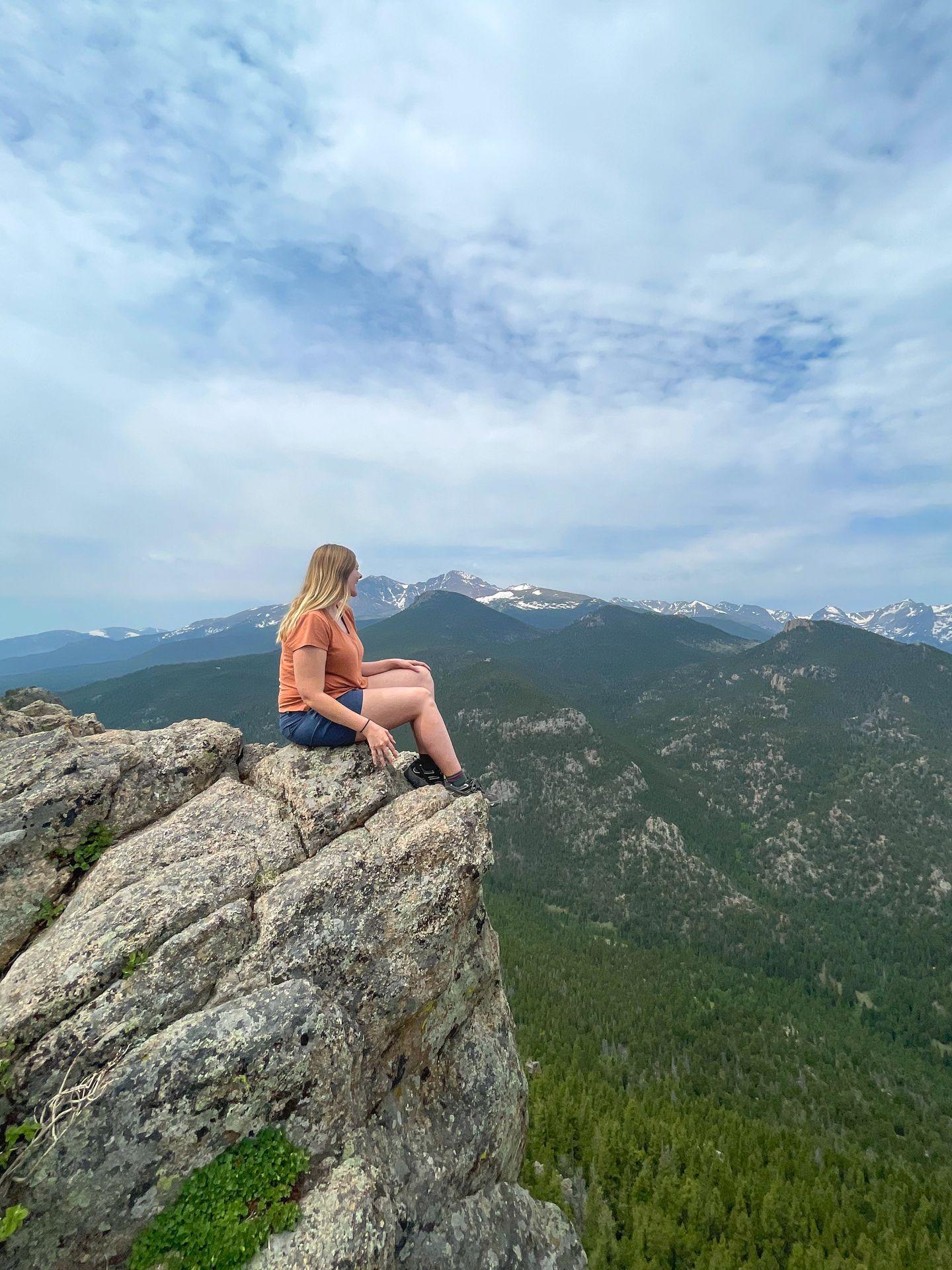 Lydia sitting on the edge of a rock and looking out at the Rocky Mountains