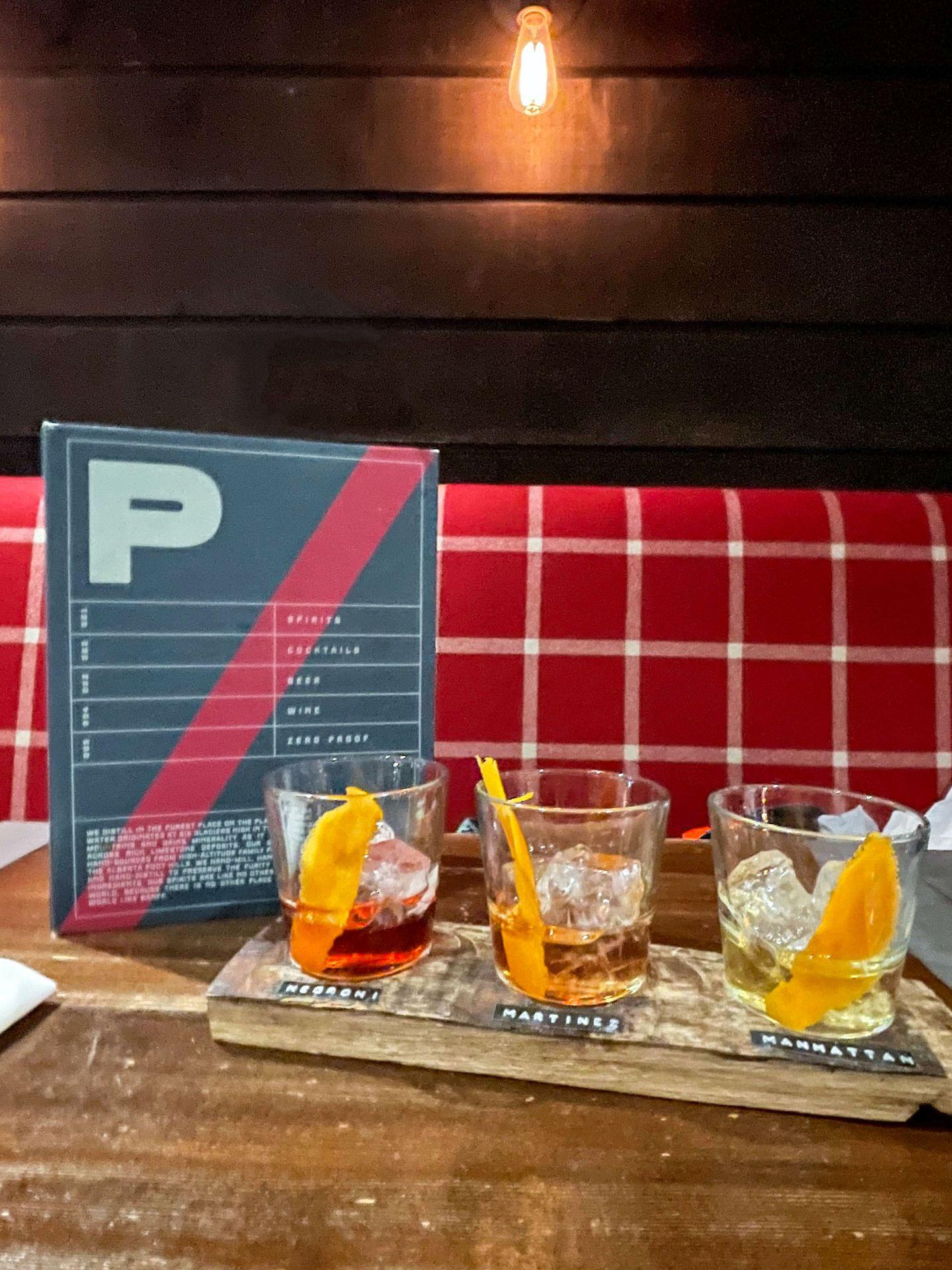 A flight of 3 cocktails next to a menu at Park Distillery.