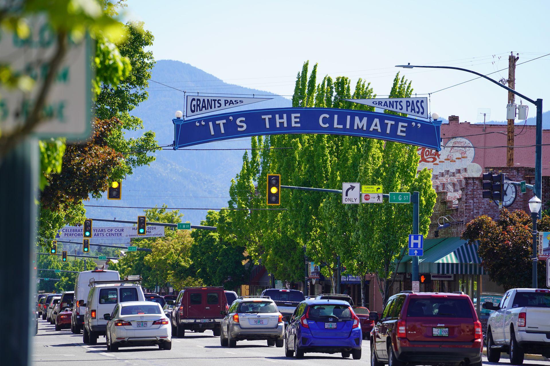 A sign going over the road that reads "It's the Climate" in downtown Grants Pass