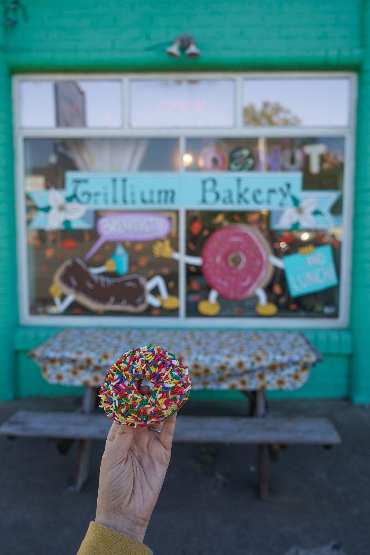 Holding up a donut with sprinkles in front of Trillium Bakery