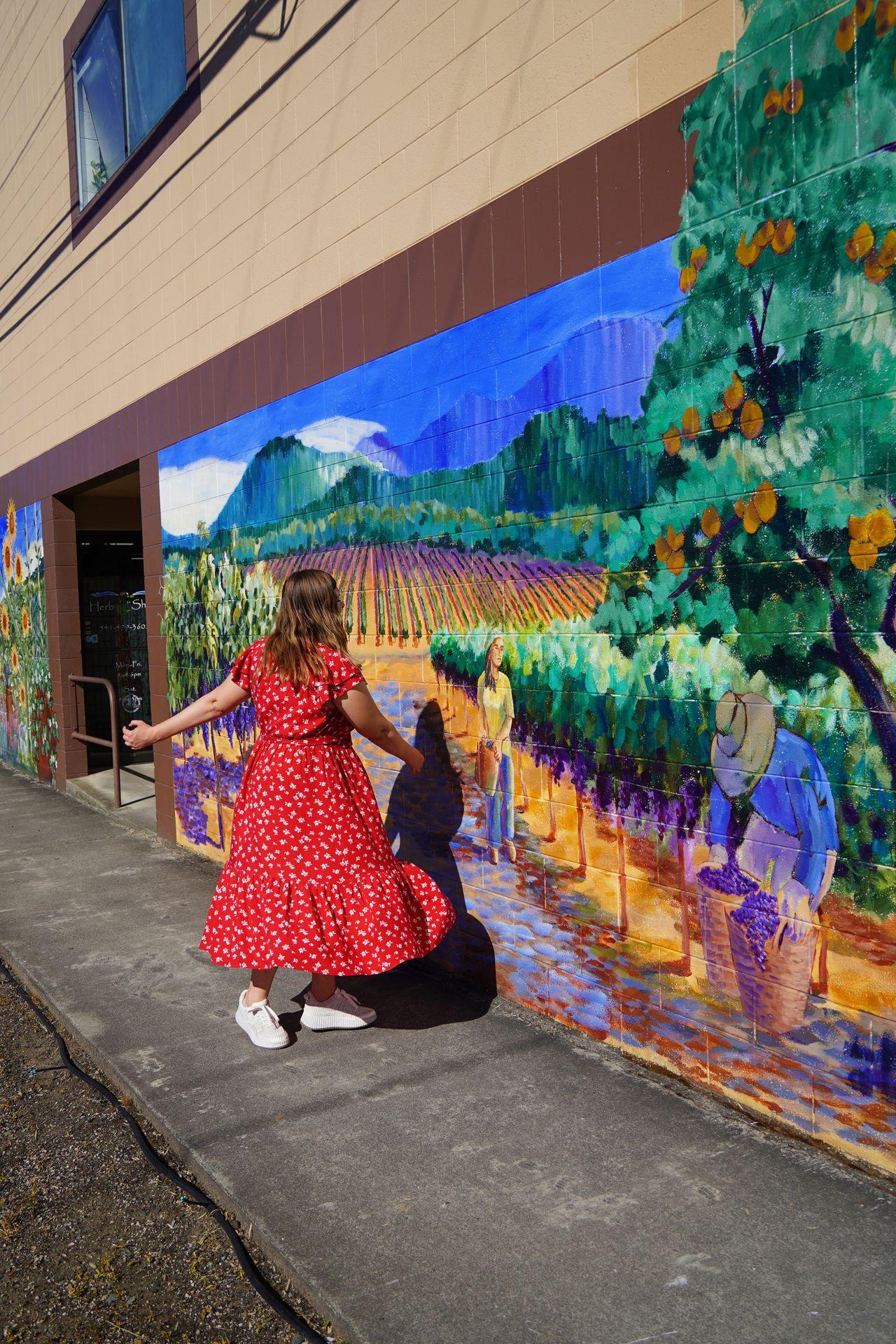 Lydia spinning in front of a mural with a rainbow vineyard, trees and mountains