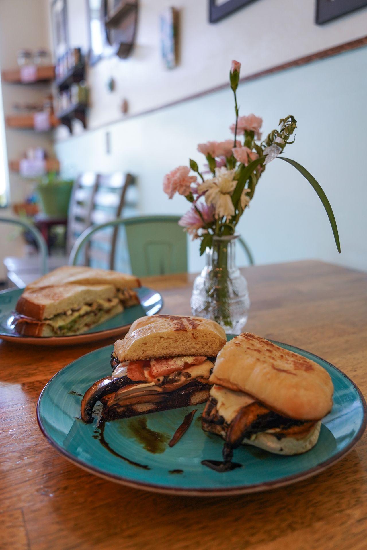 Two sandwiches next to a vase with flowers inside of Trillium Bakery