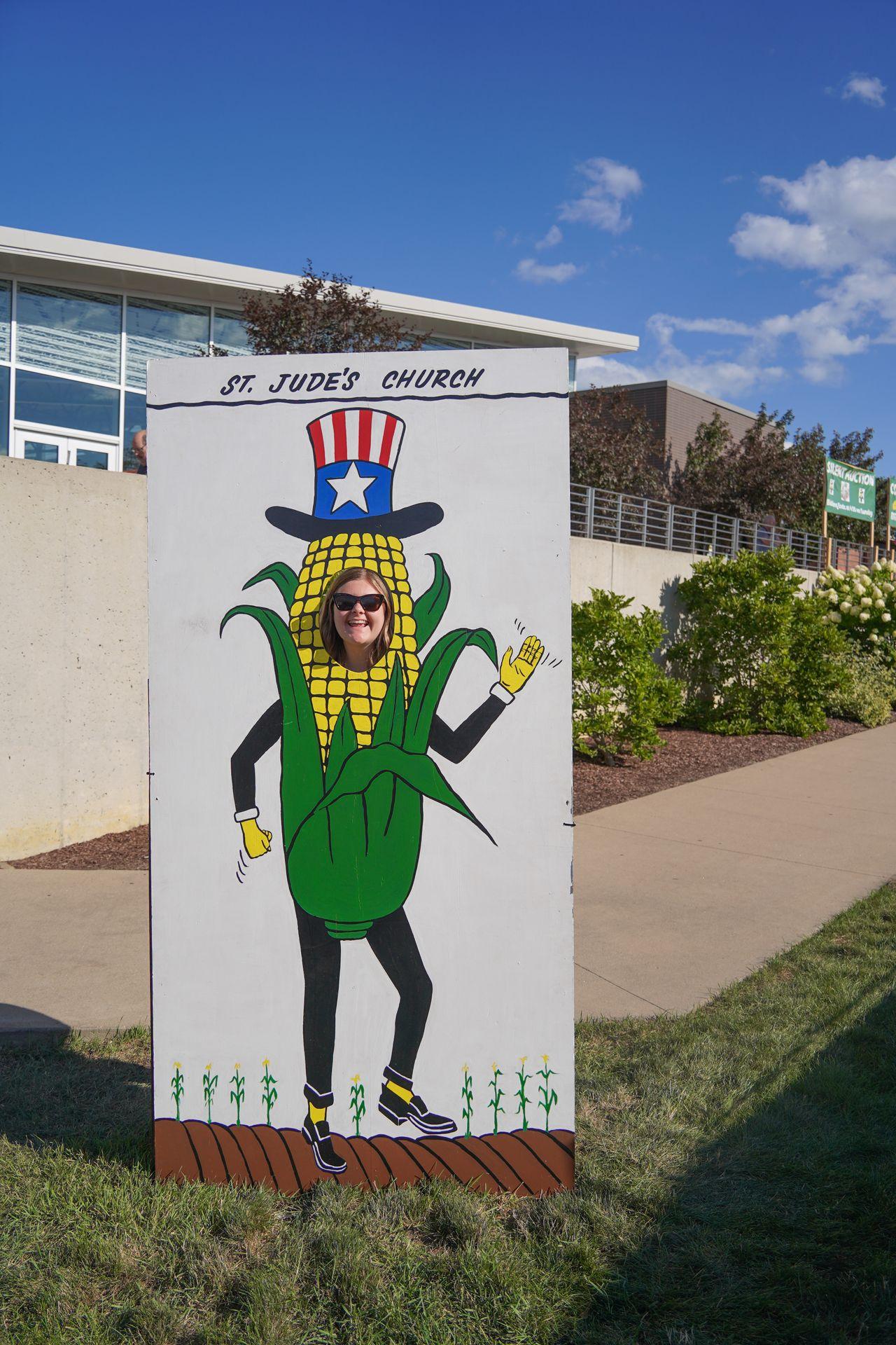 Lydia sticking her head through a corn display at the Sweet Corn Festival