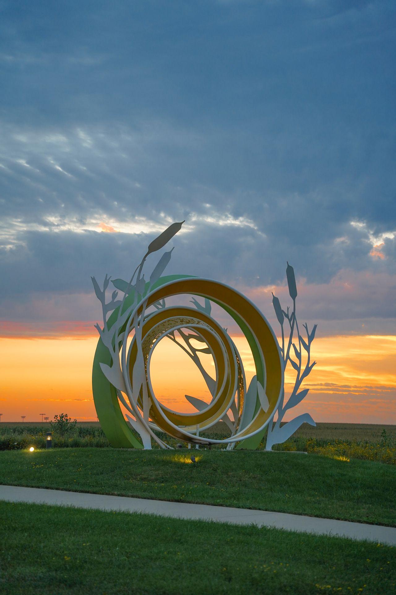 An interesting round sculpture in front of a sunset sky at Lowe Sculpture Park