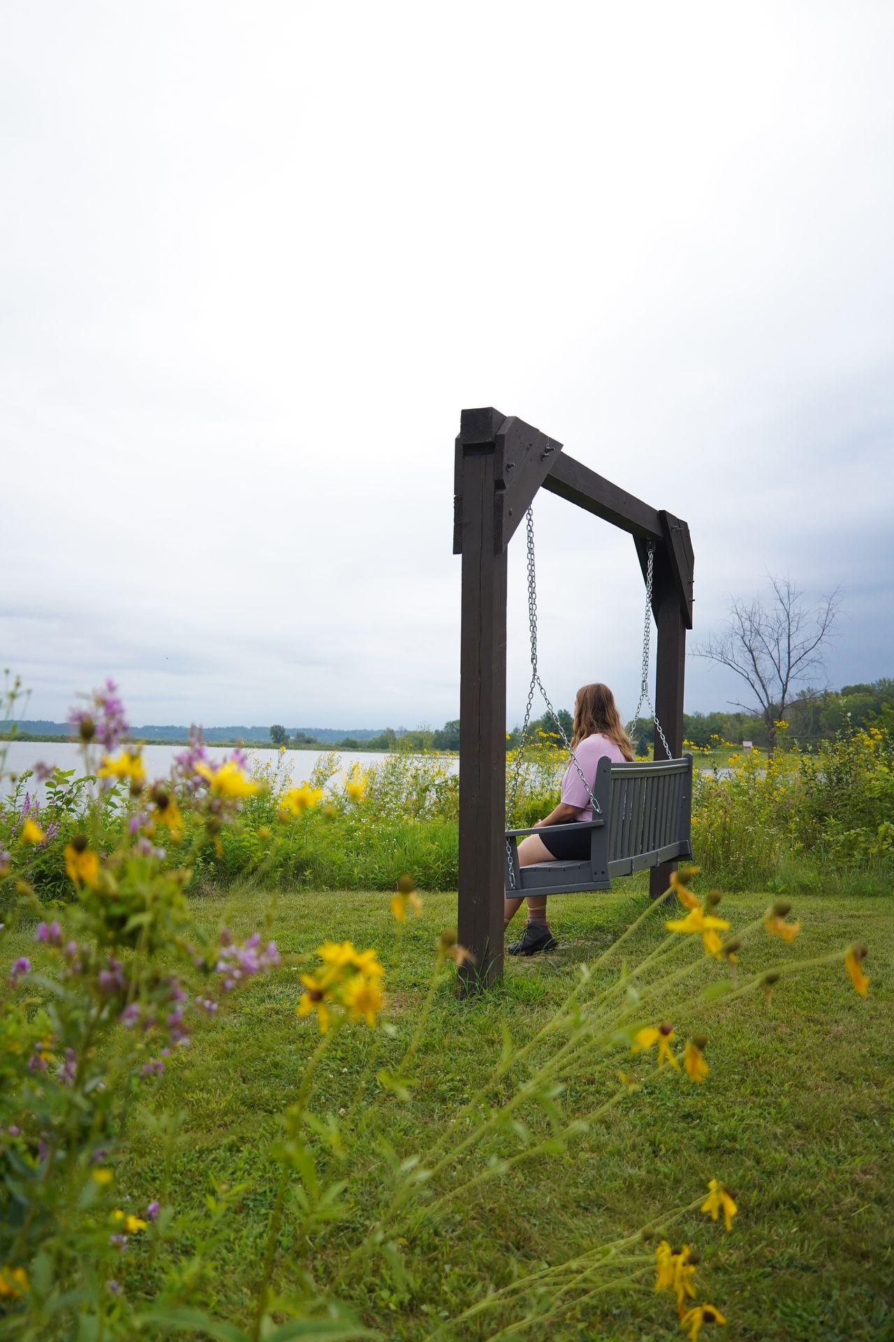 Lydia sitting on a swinging bench next to wildflowers at Pleasant Creek State Recreation Area