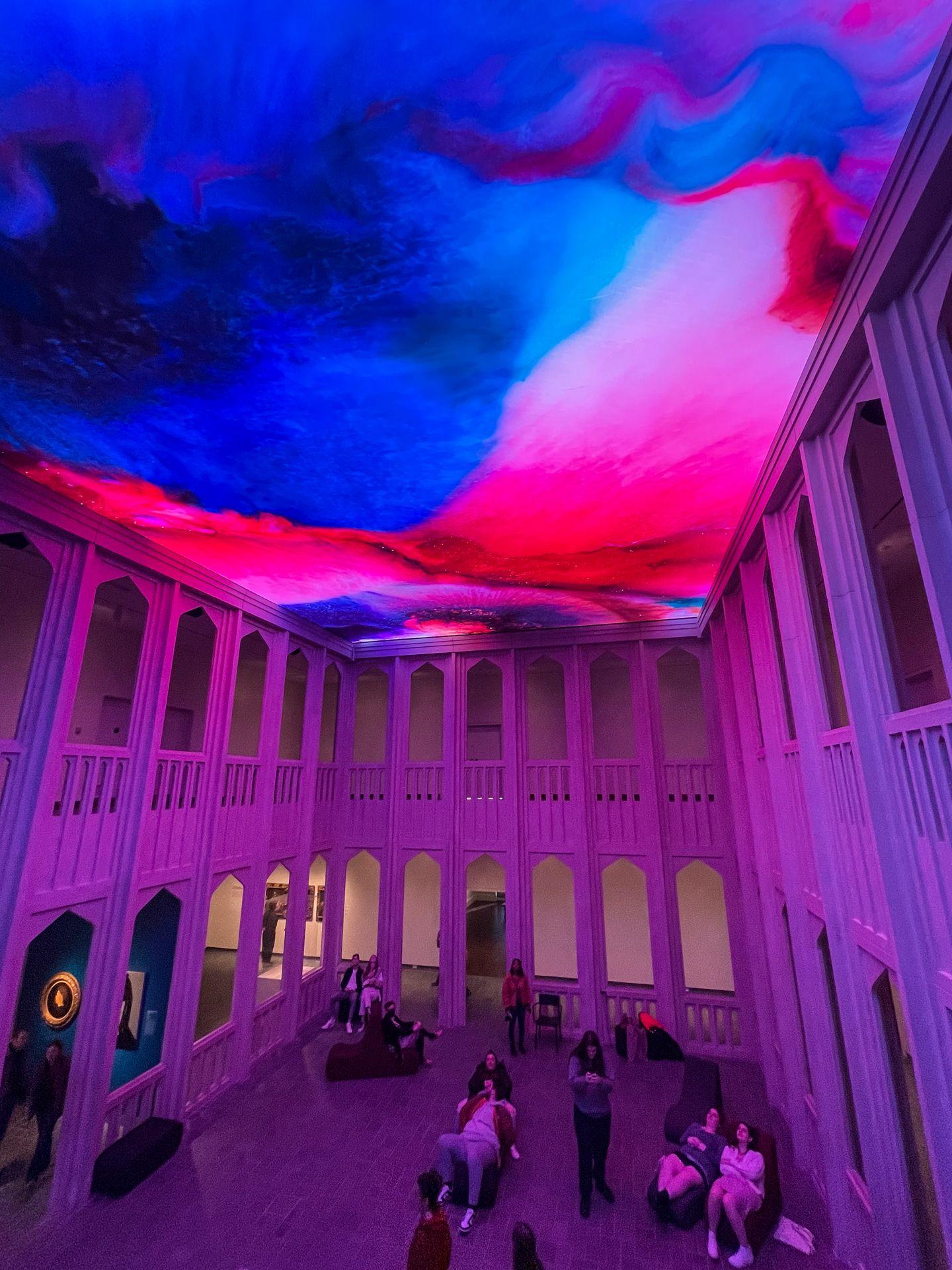 A large room with a ceiling projected in abstract blue and red colors at the Newfields Museum of Art