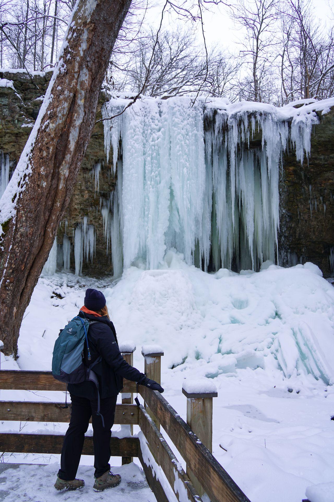 Lydia standing at a fence and gazing at a frozen waterfall