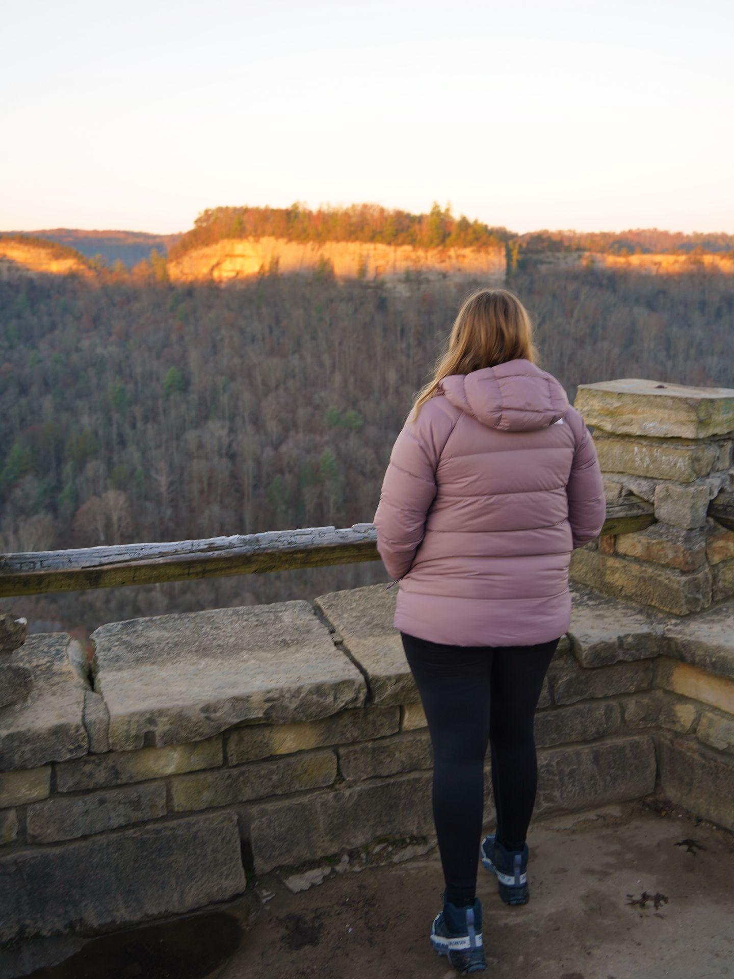 Lydia standing and looking at a valley in Red River Gorge from Chimney Top at sunrise