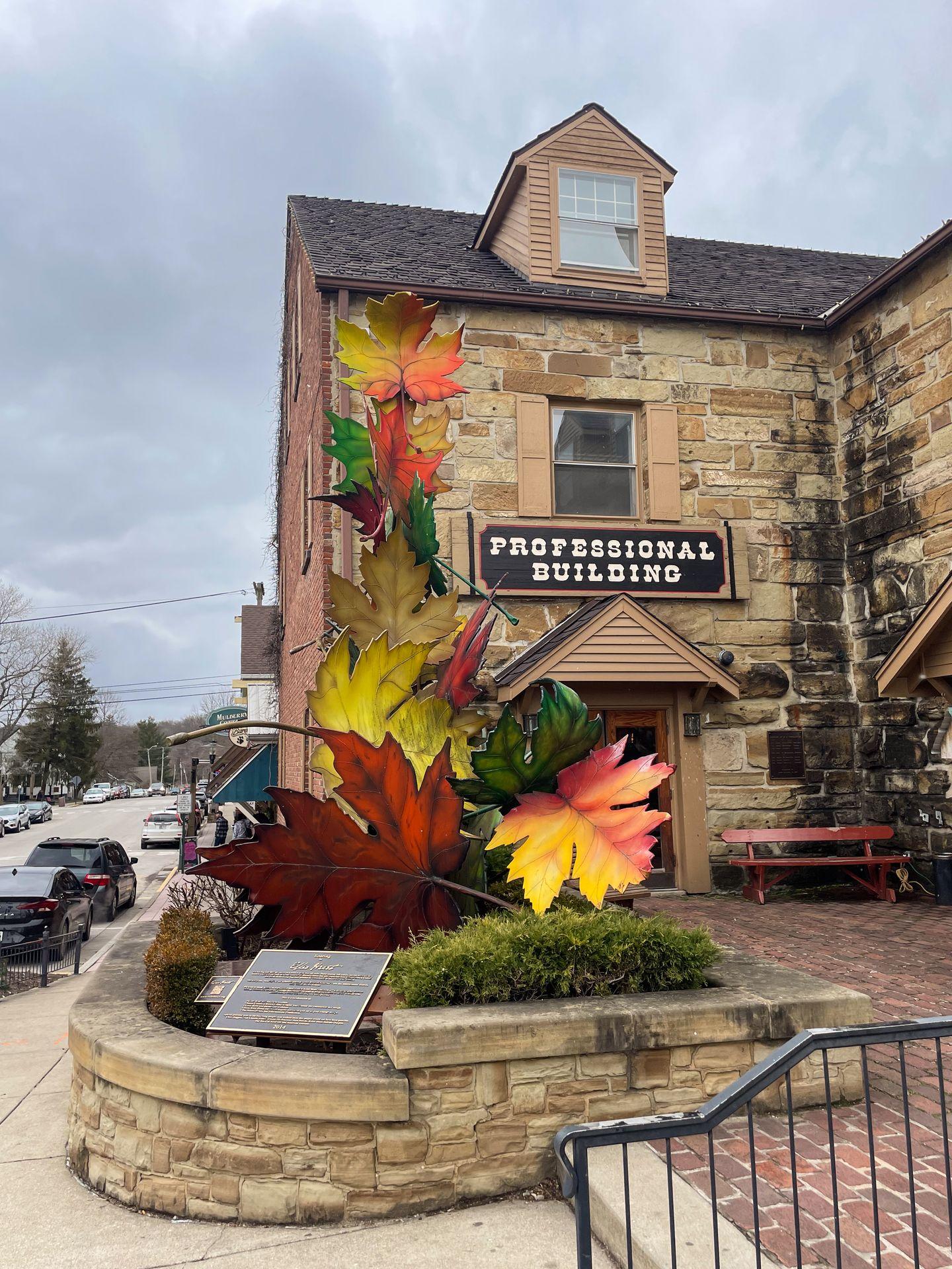 A stone building in Downtown Little Nashville. In front of the building, there is a sculpture with large fall leaves