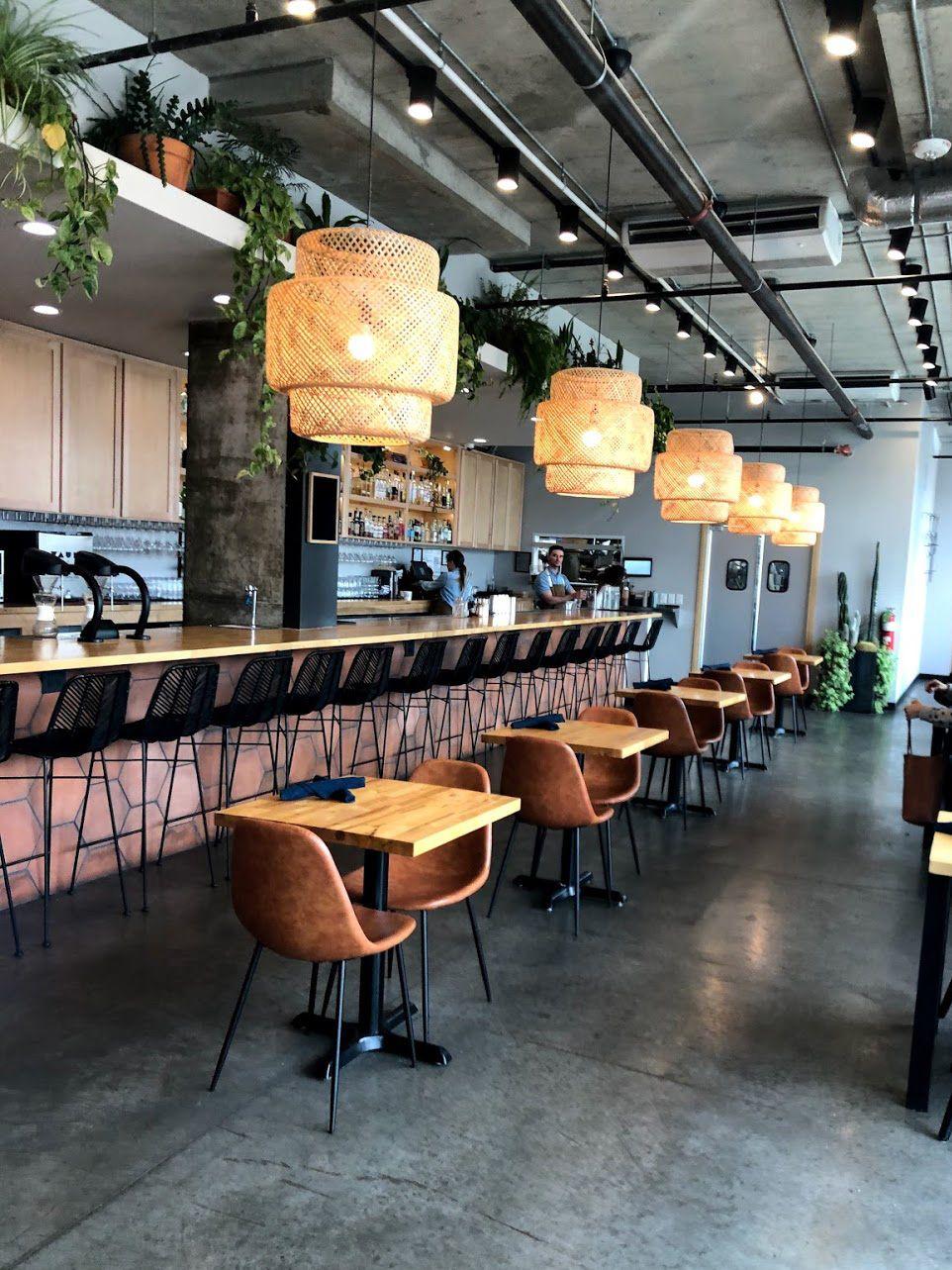 The interior of Stitch Cafe. There is a pink bar, some wood tables and some wicker hanging light fixtures.