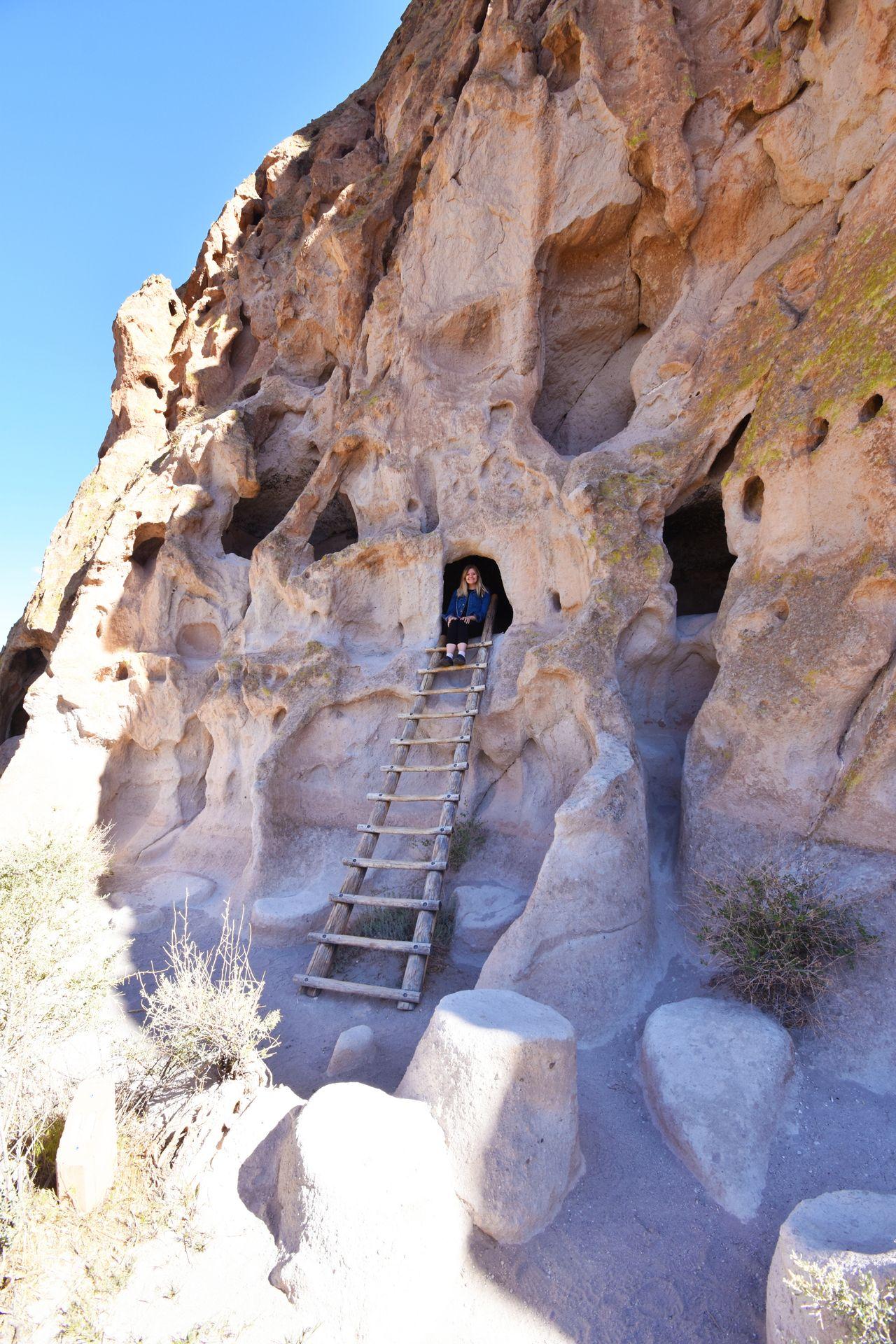 Lydia sitting in a cave above a ladder in Bandelier National Monument