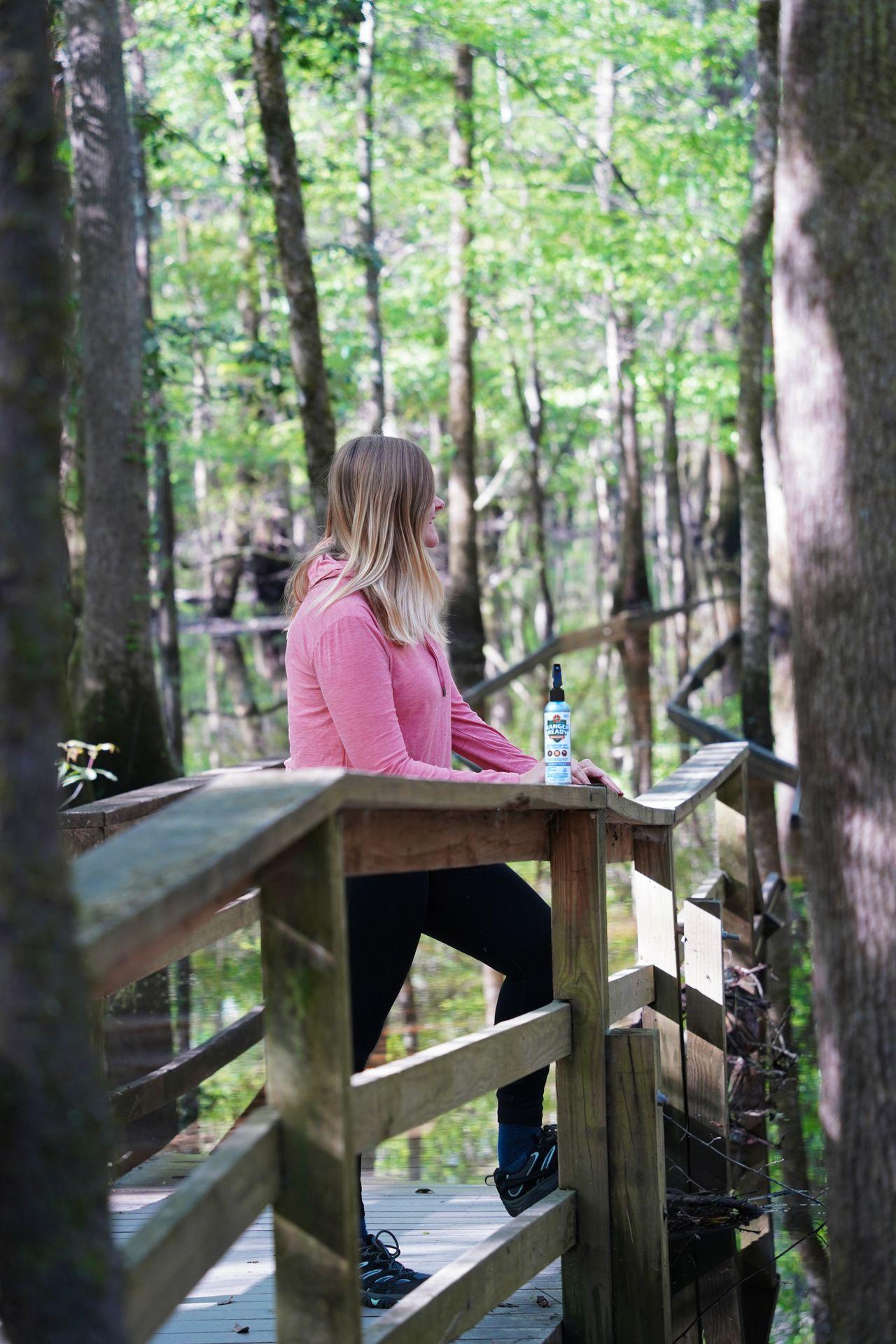 Lydia standing along the boardwalk in Congaree National Park with bug spray sitting on the fence