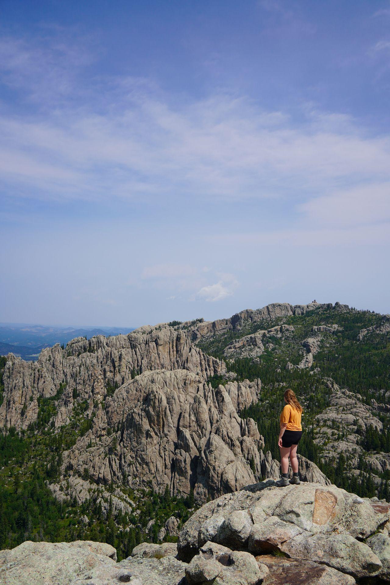 Lydia standing and looking out at a view of rocks and trees from Little Devil's Tower in Custer State Park