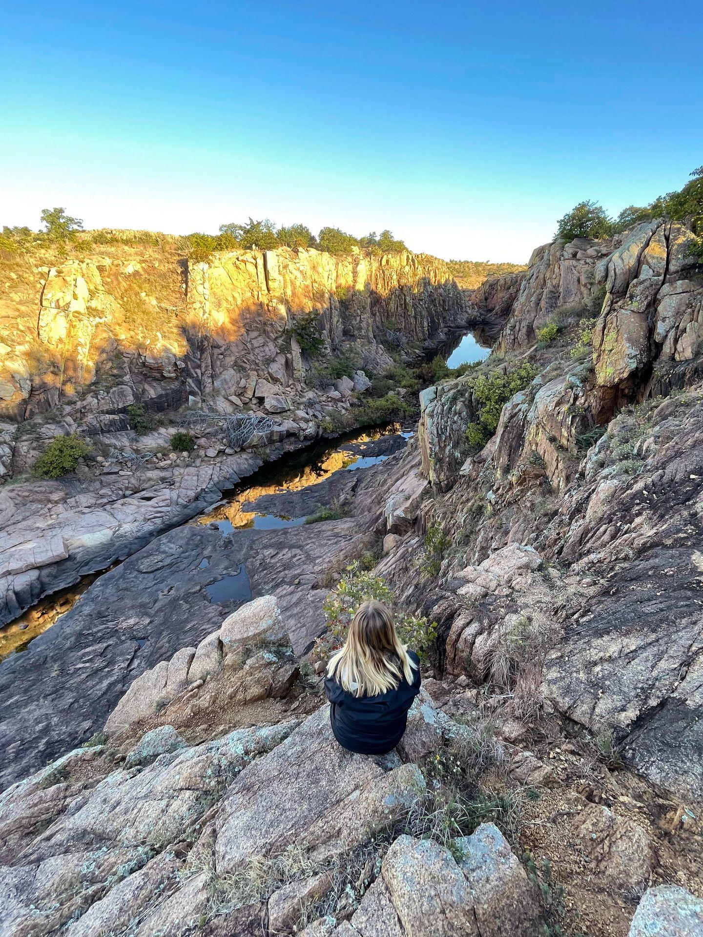 Lydia sitting and looking out a view of water and rocks along the Fort Foot Hole trail.