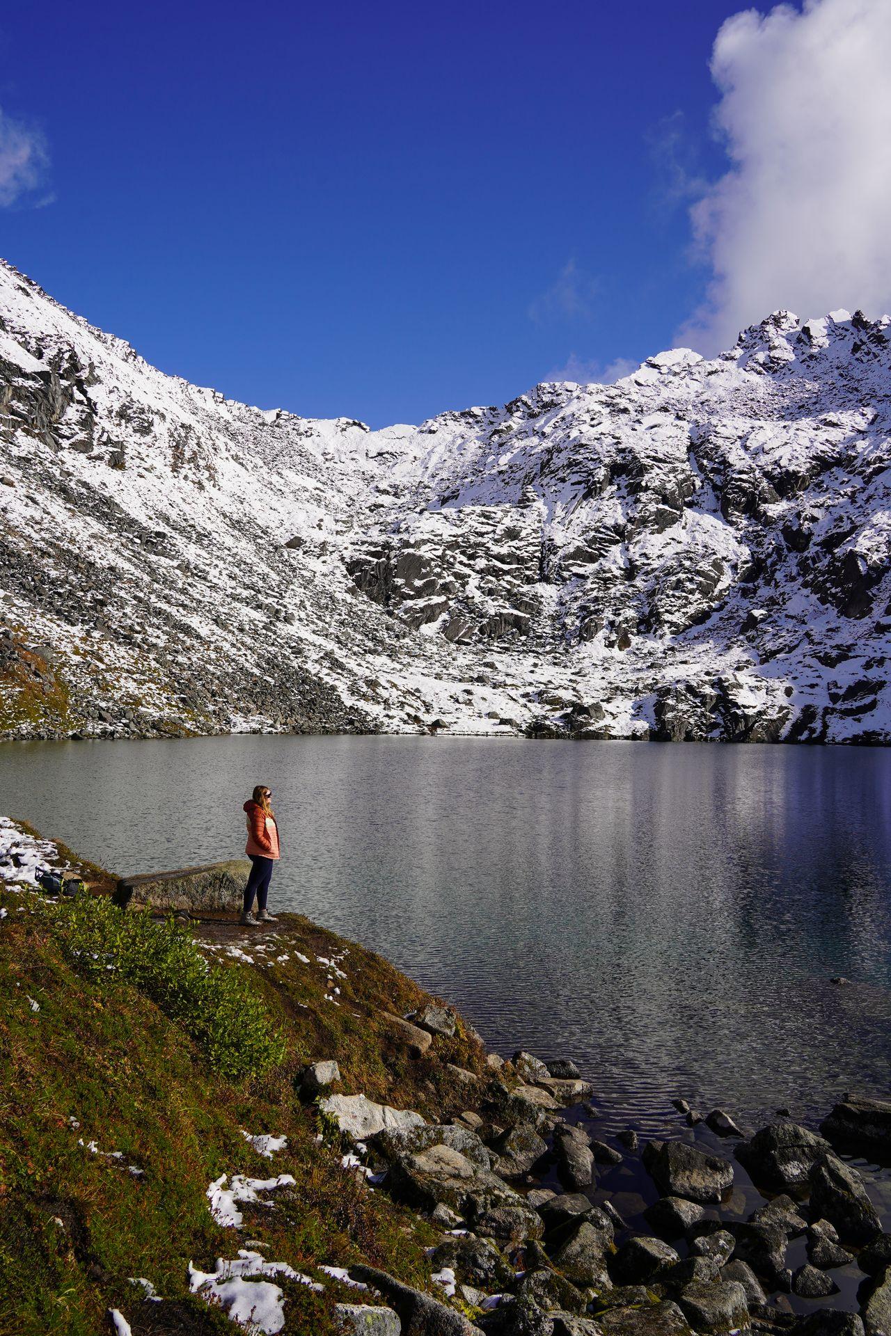 Lydia standing on the edge of a lake. In the background there is a mountain covered in snow