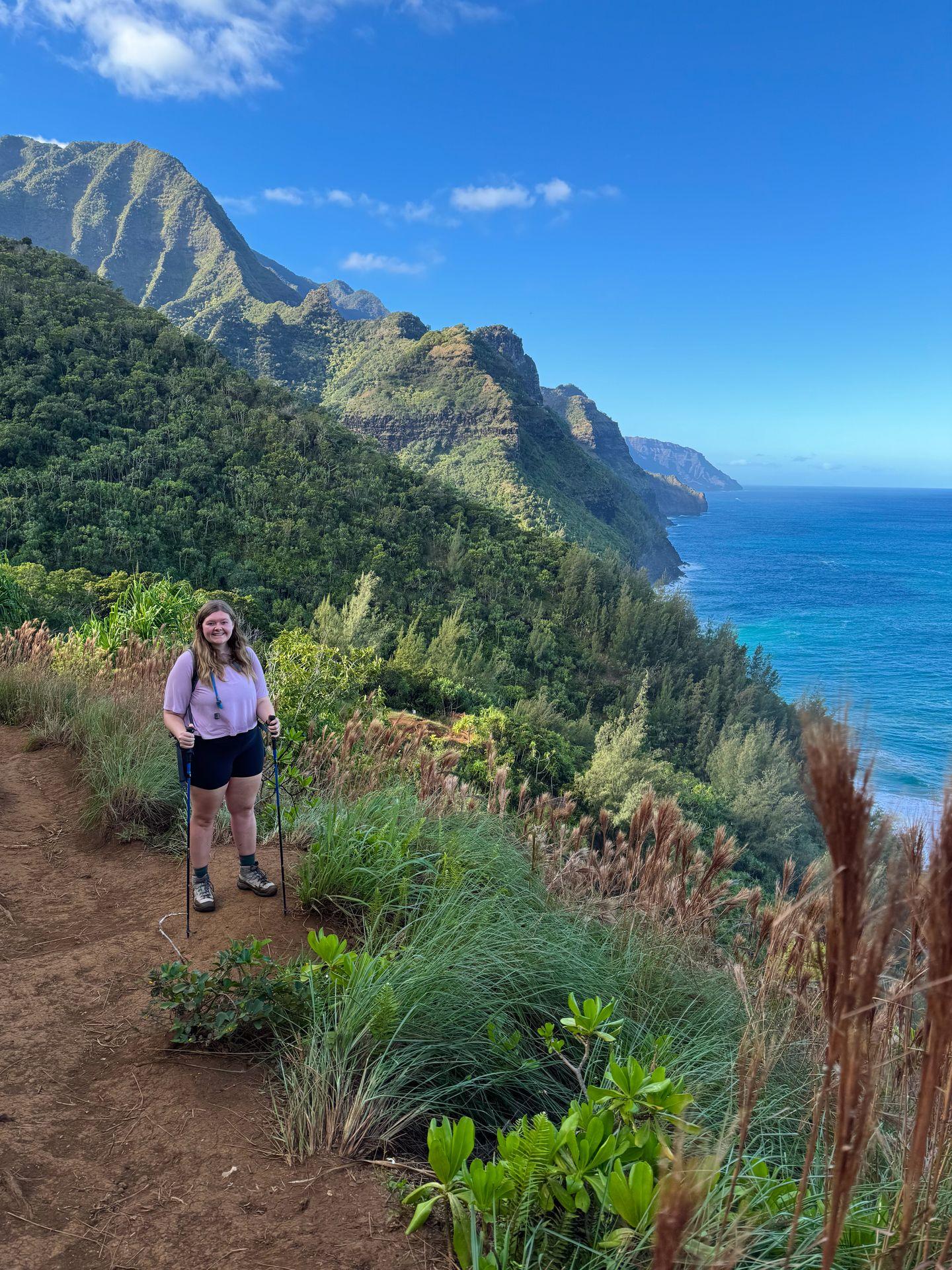 Lydia standing on a trail with the Na Pali Coast in the background