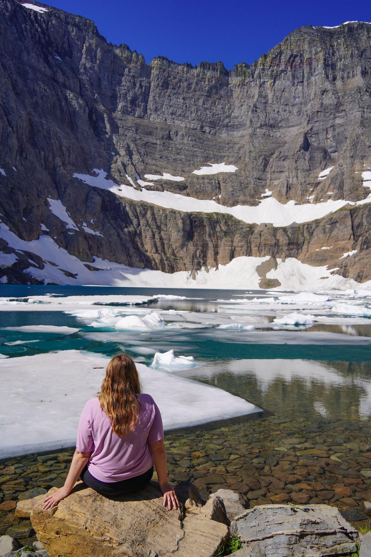 Lydia sitting and looking out at a blue lake with icebergs floating in it