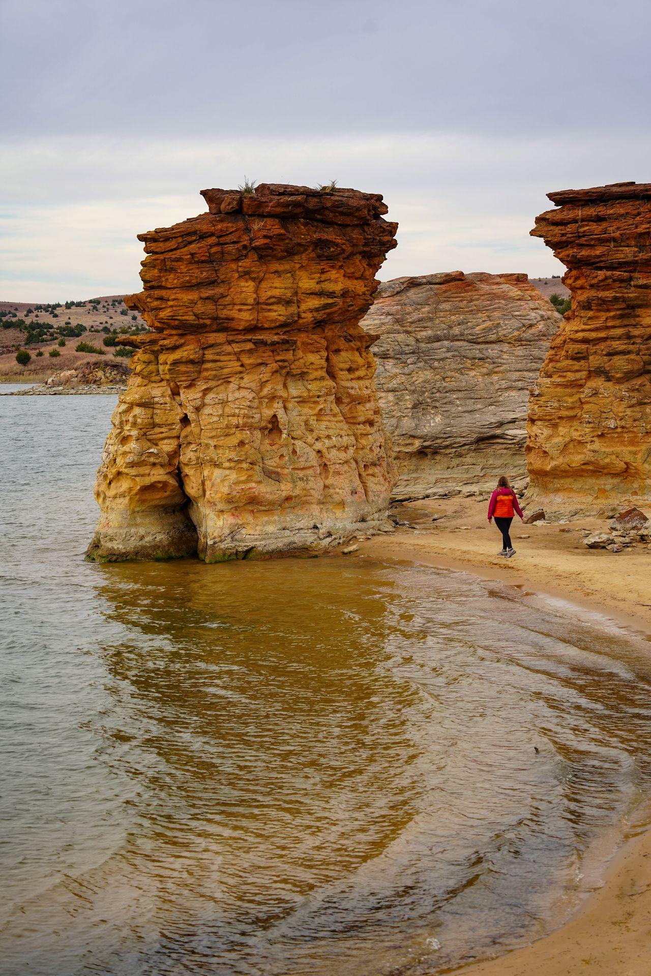 Lydia walking towards huge rocks next to the water on the Rock Town Trail