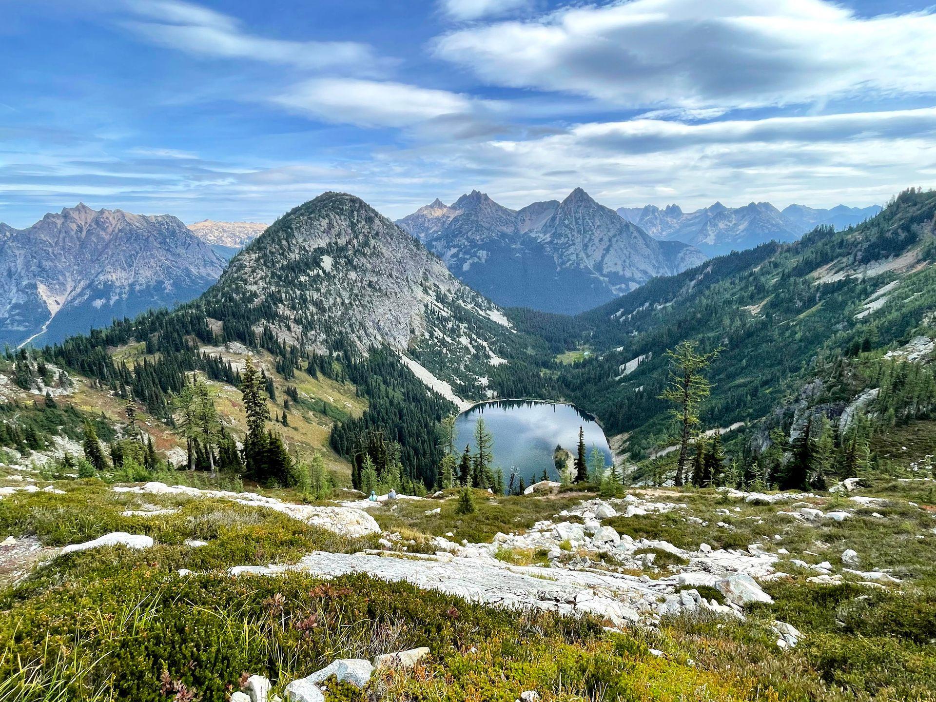 An expansive view with mountains covered in greenery and a small lake at the bottom of the valley