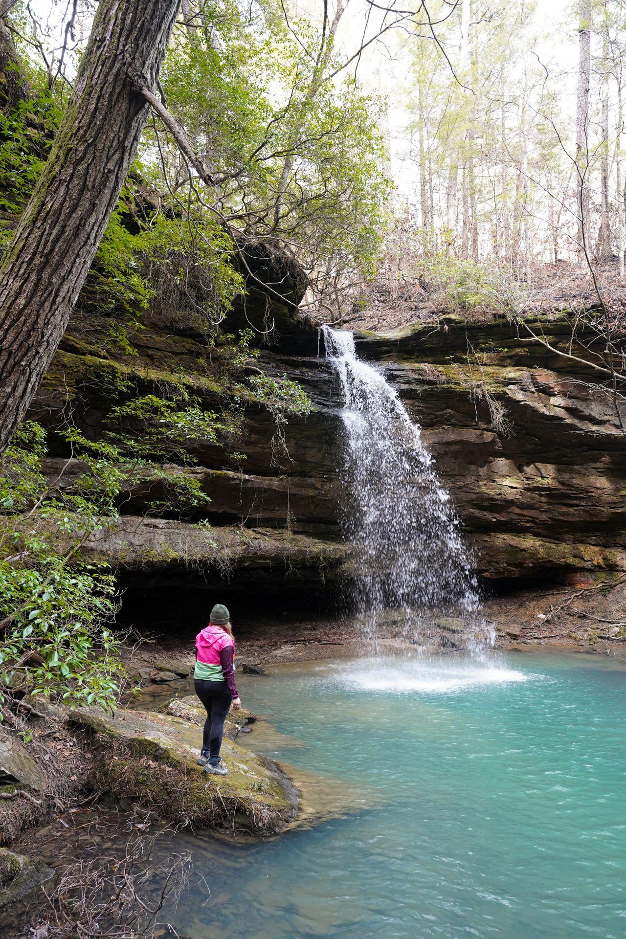 Lydia looking at a waterfall next to a aqua-blue pool of water