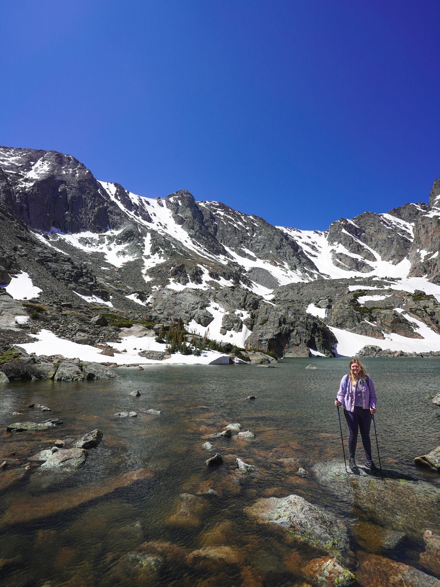 Lydia sitting next to Sky Pond. There are various drifts of snow along the mountainside.