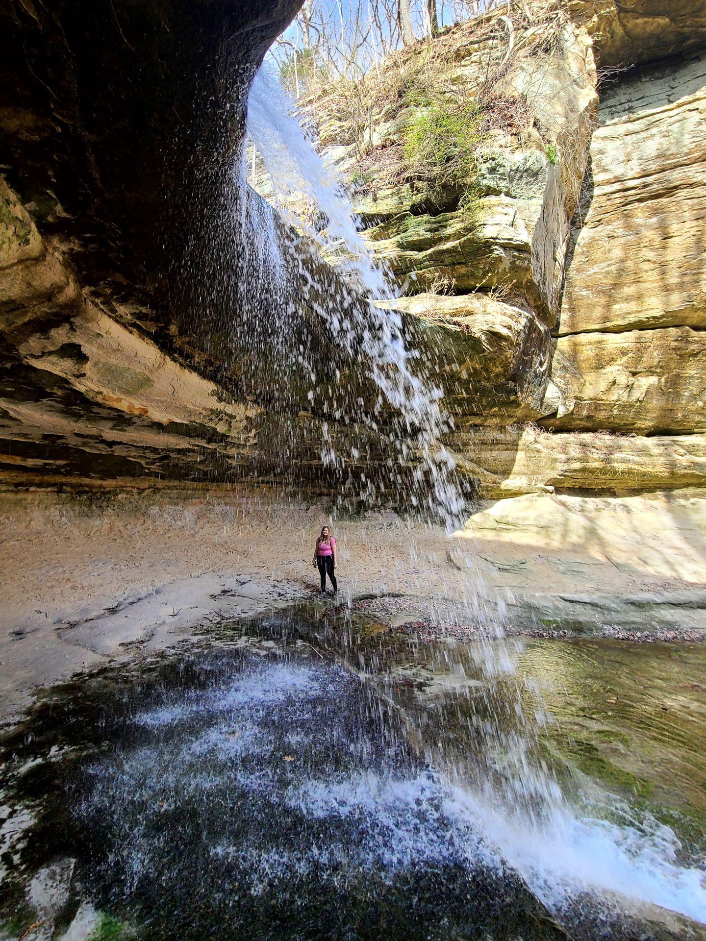 Lydia standing on the opposite side of a waterfall in Starved Rock State Park