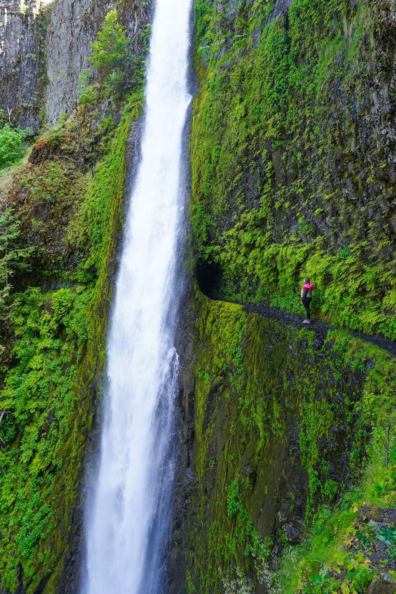 Lydia standing next to a tall waterfall that has a tunnel behind it.