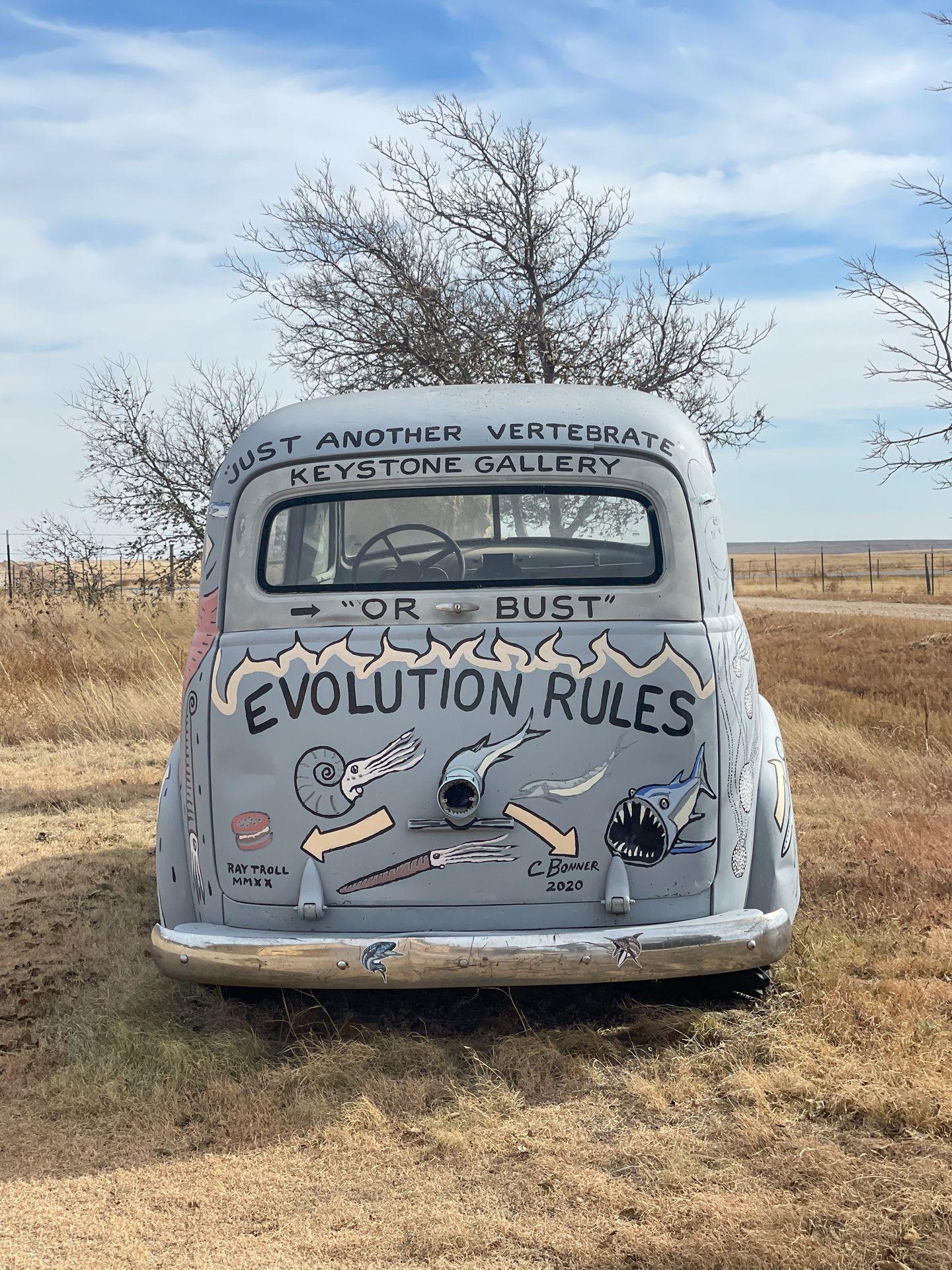 A painted car outside of the Keystone Art Gallery. One phrase reads 'Evolution Rules'