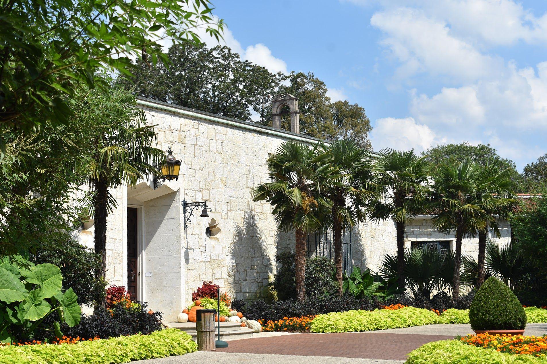 A white building with palms and greenery at the Dallas Arboretum.