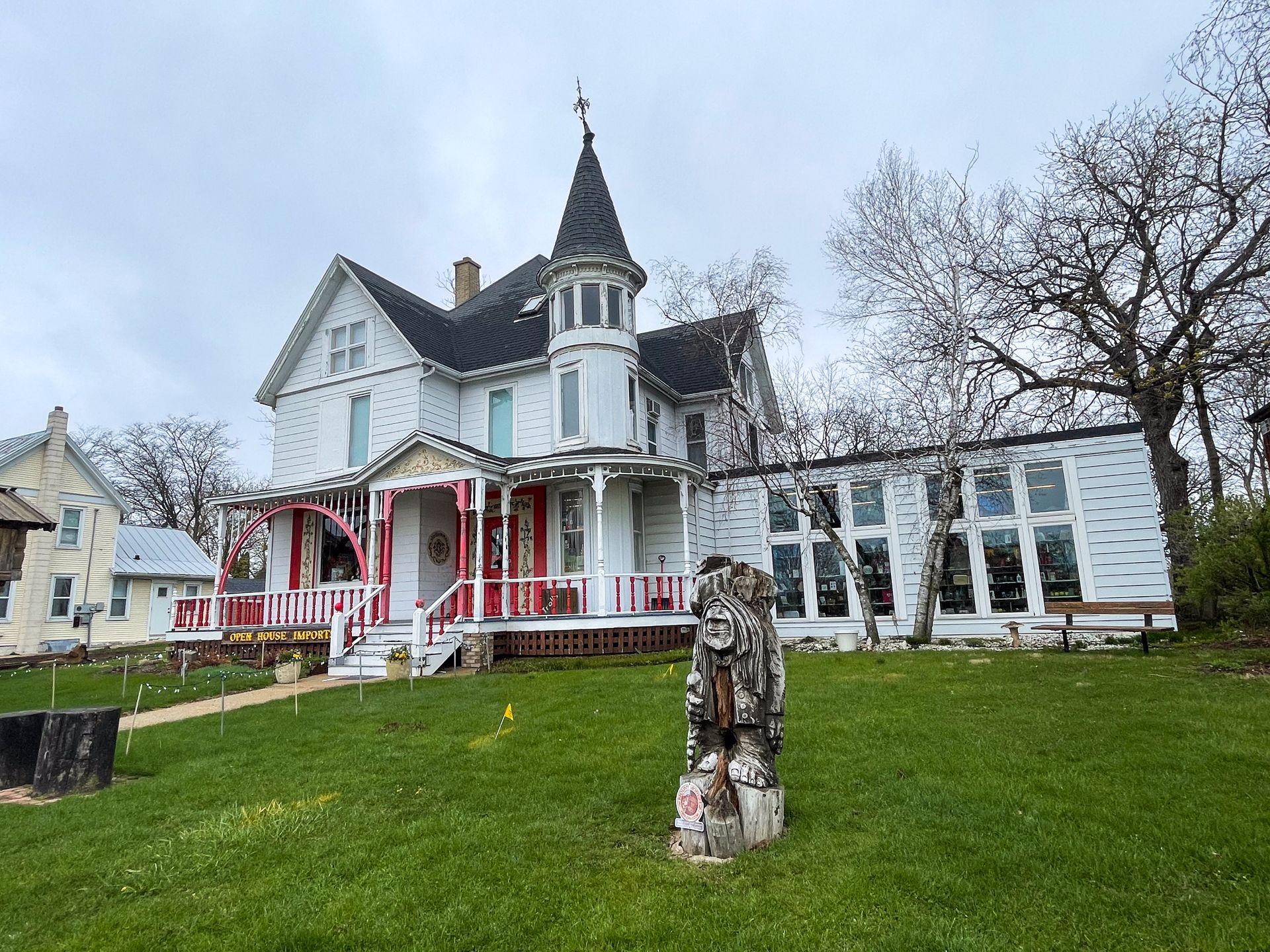 The exterior of Open Source Imports. It's a white building that looks like a historic home. A troll statue is in the lawn in front of the shop.