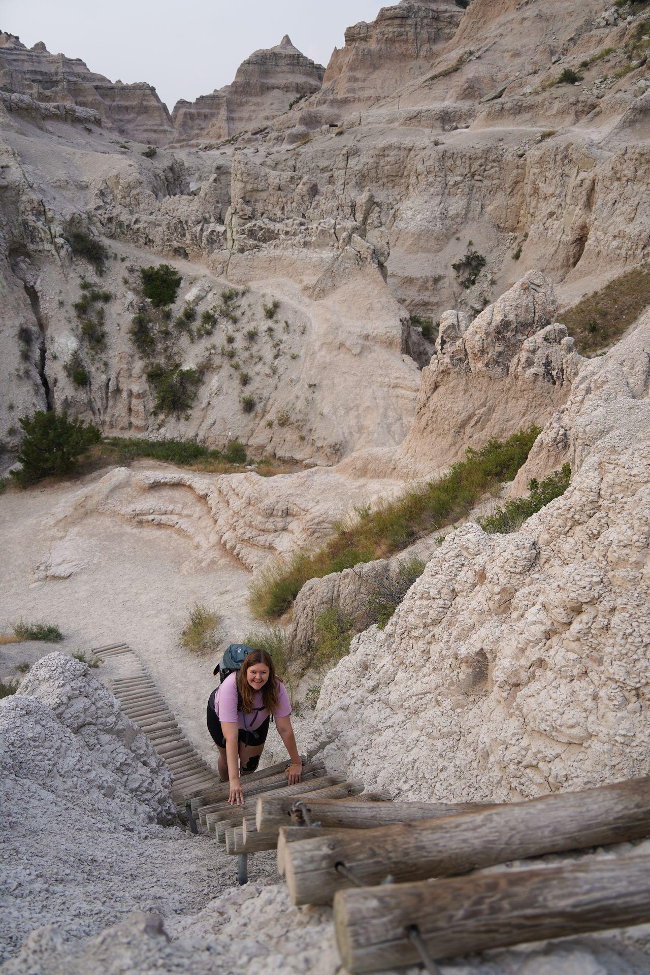 Lydia climbing up a wooden ladder on The Notch Trail at Badlands National Park