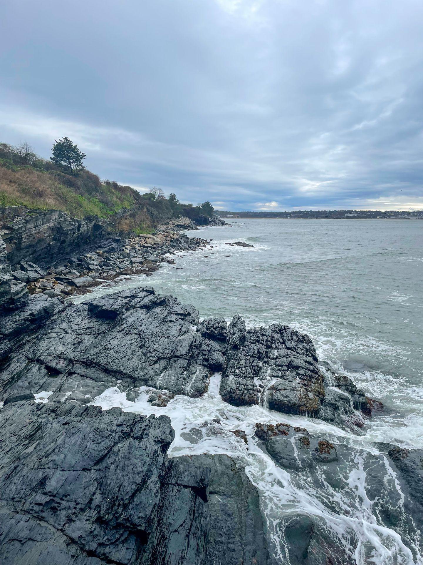 Black, smooth rocks on the shore of the ocean in Newport, Rhode Island.