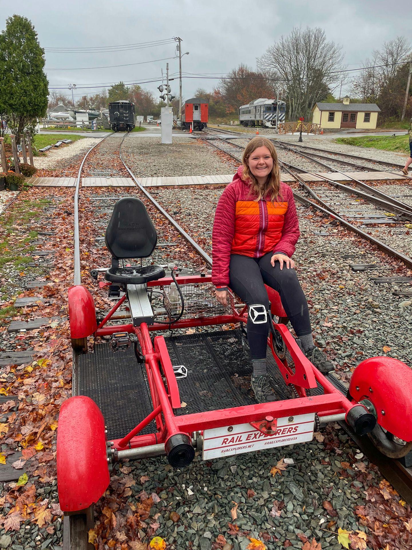 Lydia sitting on a Rail Explorers bike parked on railroad tracks.