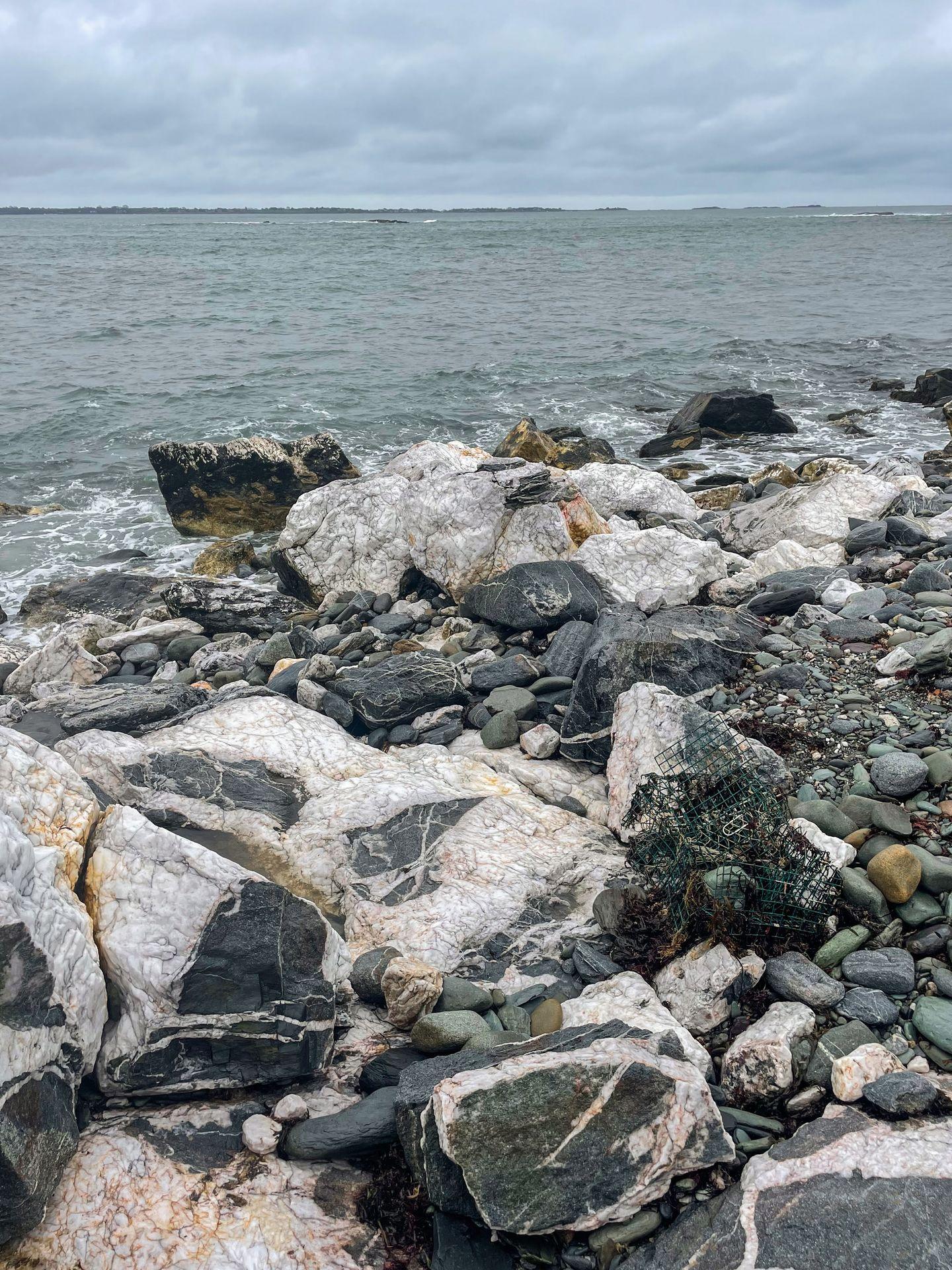 An area of black and white rocks with a bit of a stripe pattern next to the ocean.