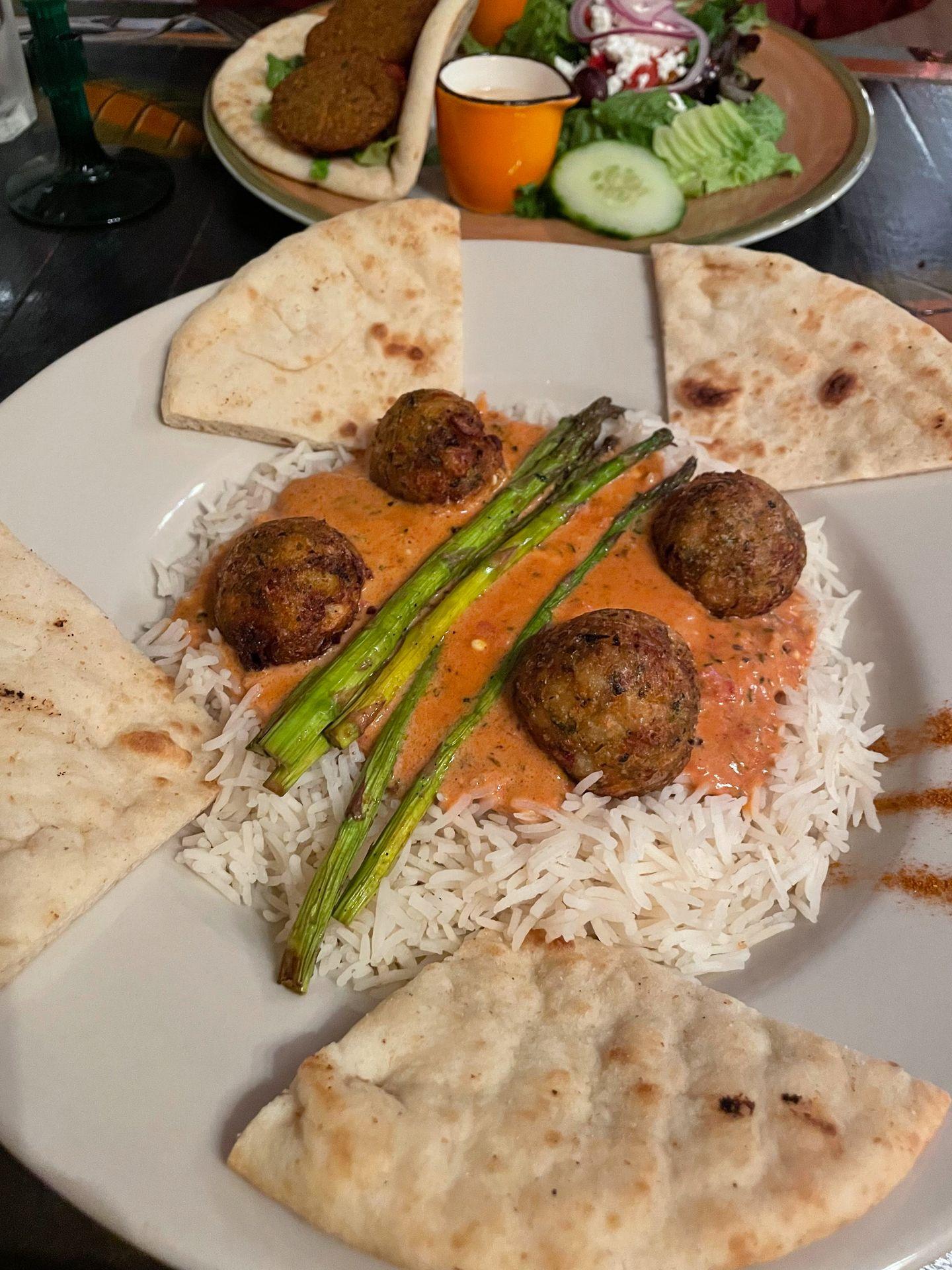 A dish of Malai Kofta from Gypsy Cafe. The meal includes rice, vegetarian meatballs, asparagus and pita bread.