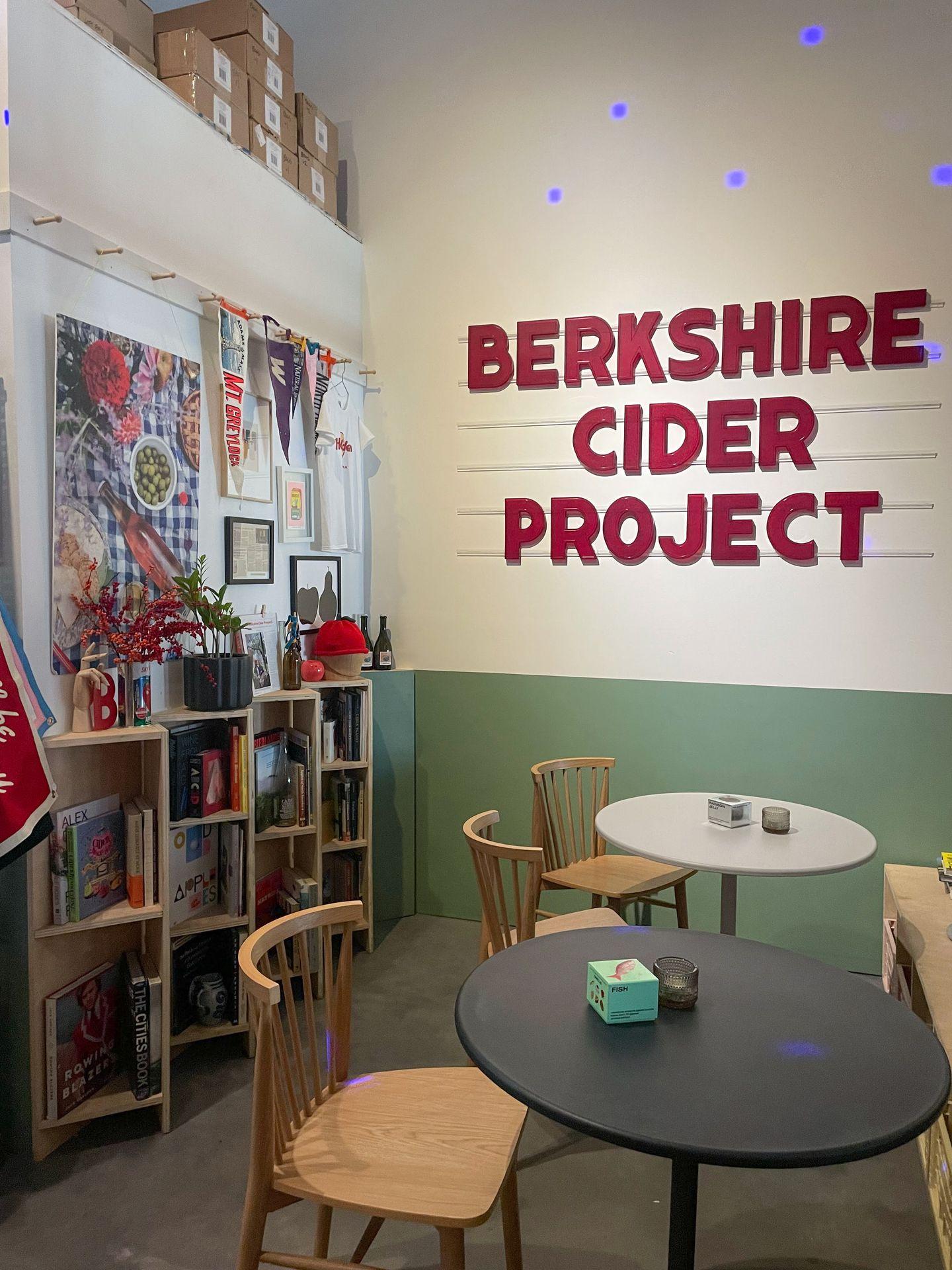 Inside of the Berkshire Cider Company shop. The wall is green and white, there is a round table and shelves full of books