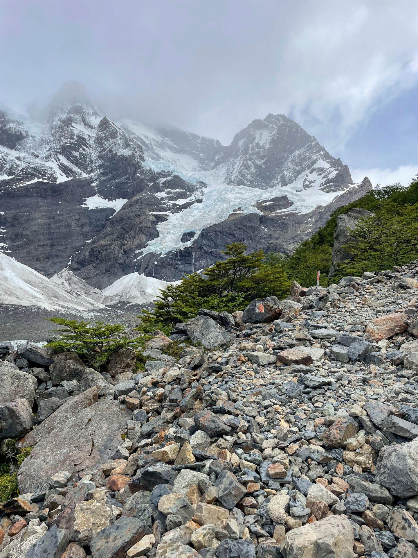 A rocky trail with a view of mountains full of glaciers in the distance.