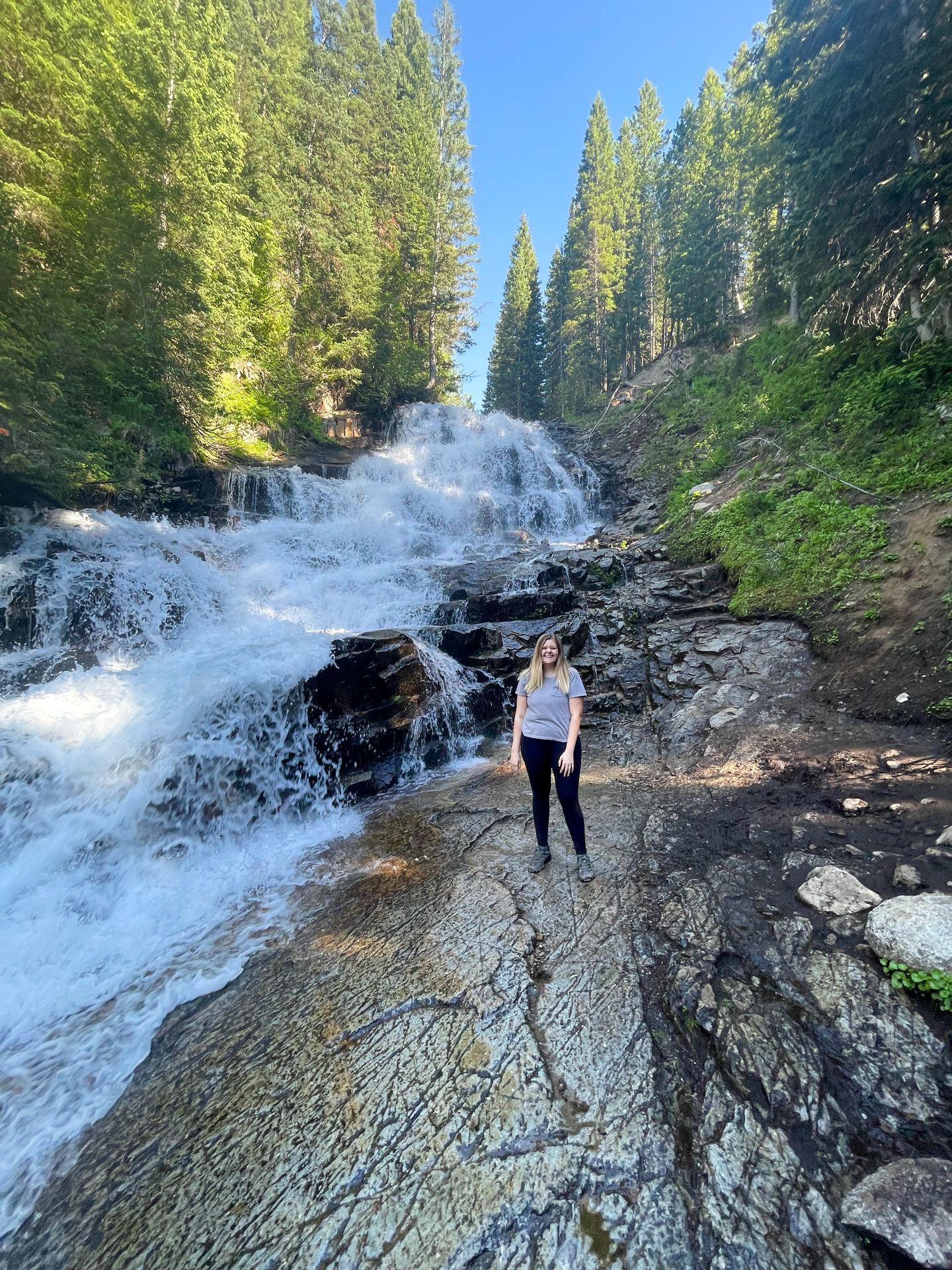 Lydia standing in front of a waterfall surrounded by green trees.