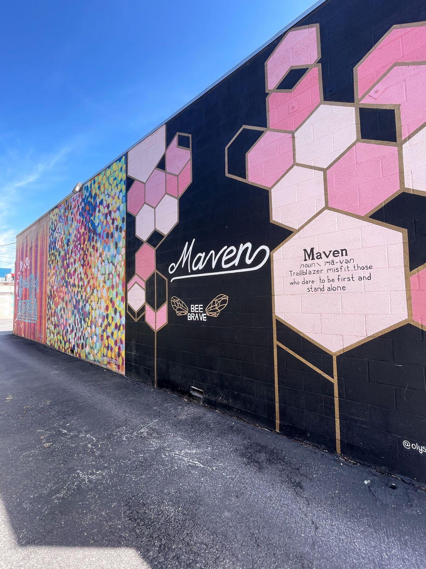 A wall of murals in the Maven District. The closest reads 'Maven' in pink letters on a black wall