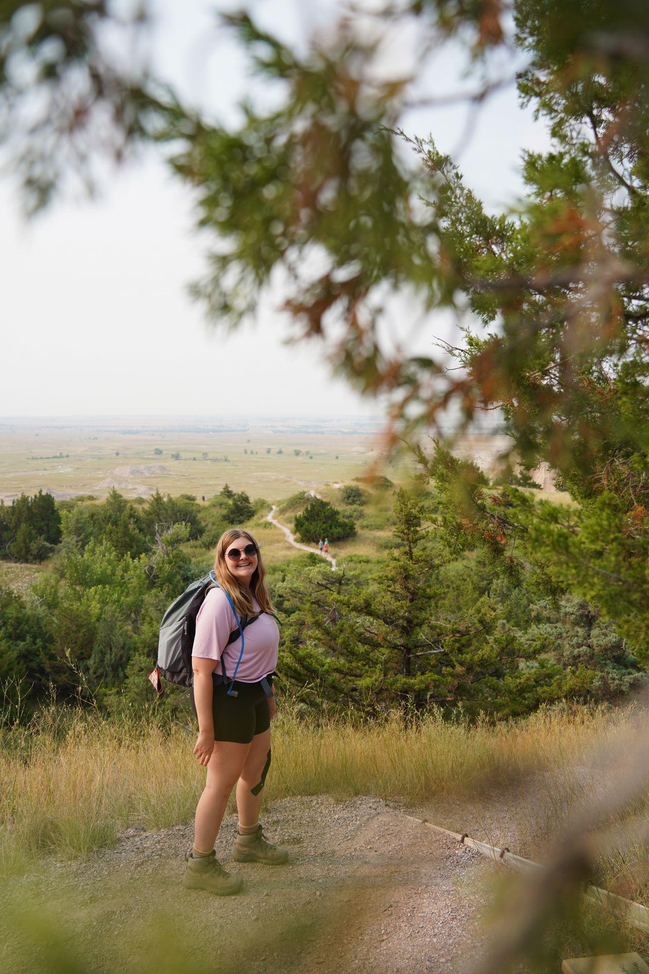 Lydia on the Cliff Shelf Nature Trail, seen through blurred green tree branches