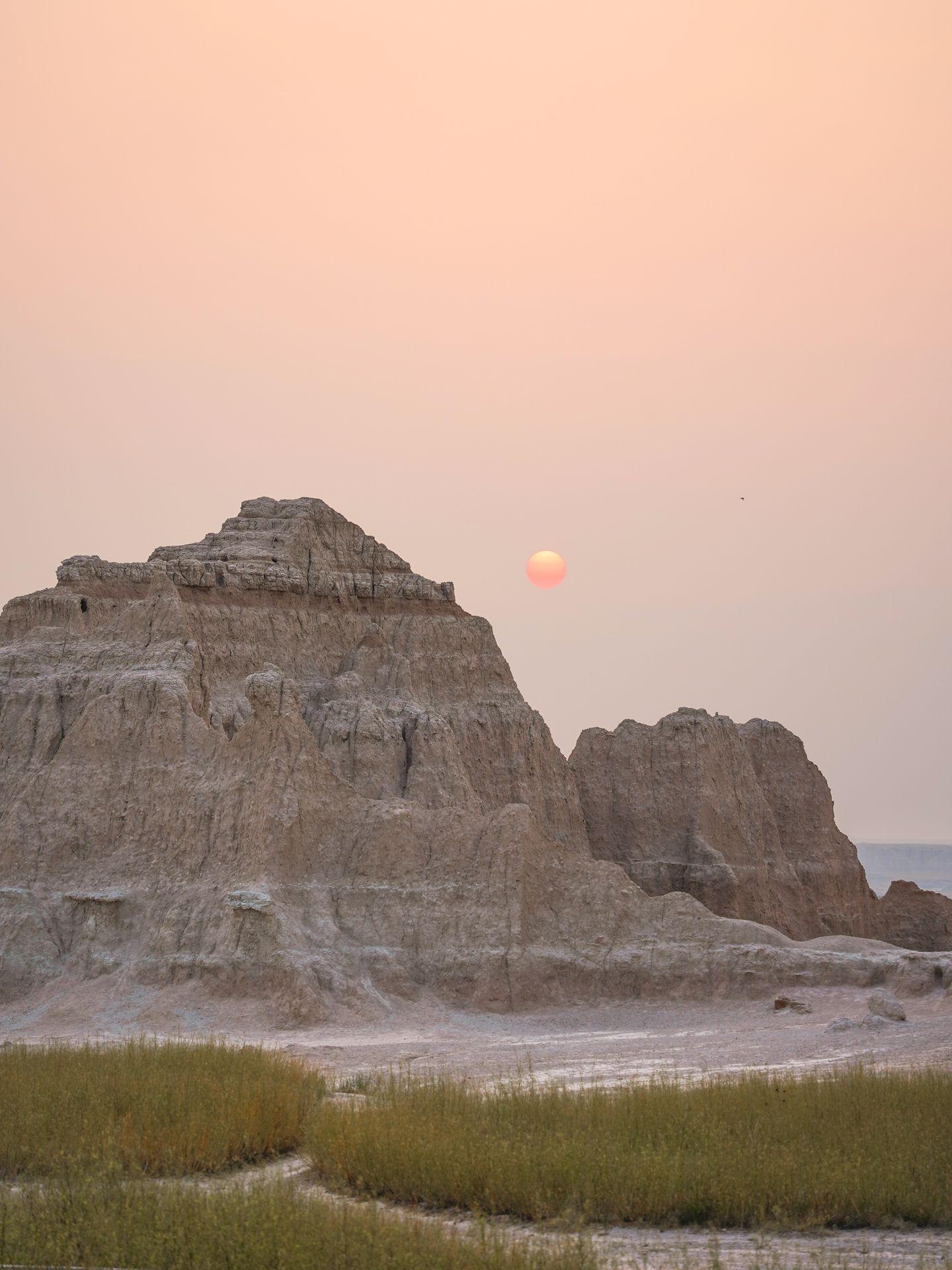 A hazy sun at sunrise next to jagged rocks in the Badlands