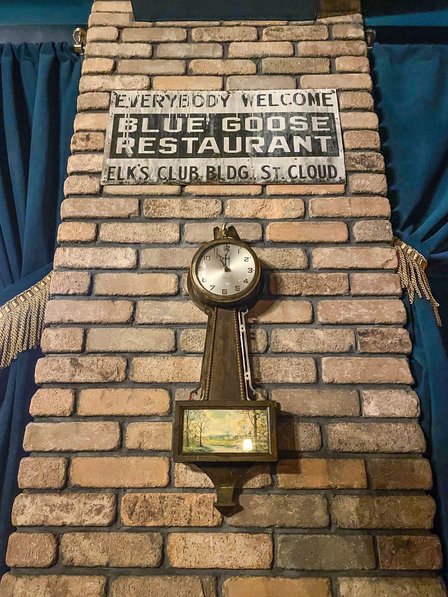 A clock and a vintage-looking sign on a brick wall in the Blue Goose Speakeasy