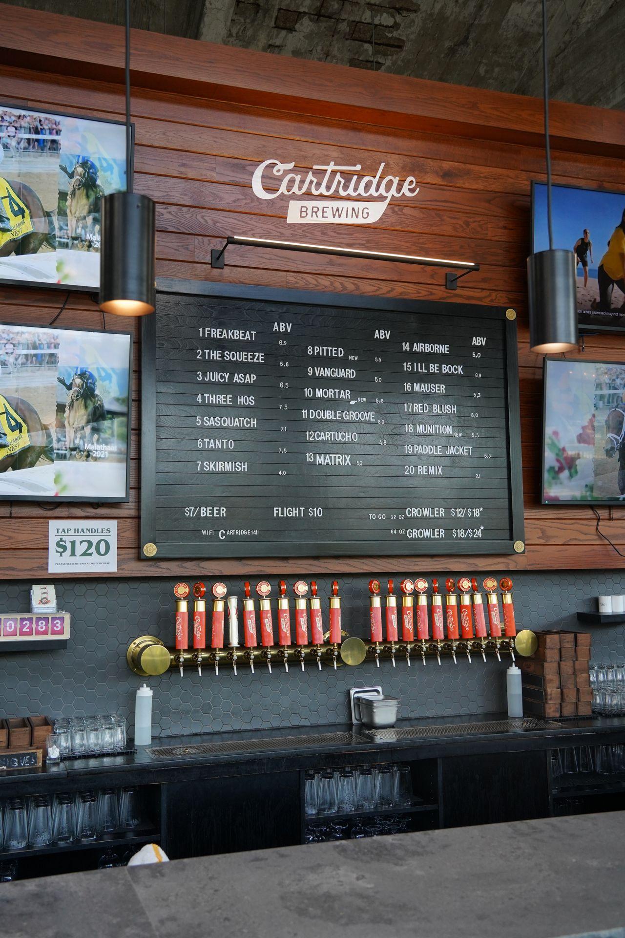 The taps at Cartridge Brewing. There is a wooden wall with a black message board lisiting the beers, and the taps are all orange.