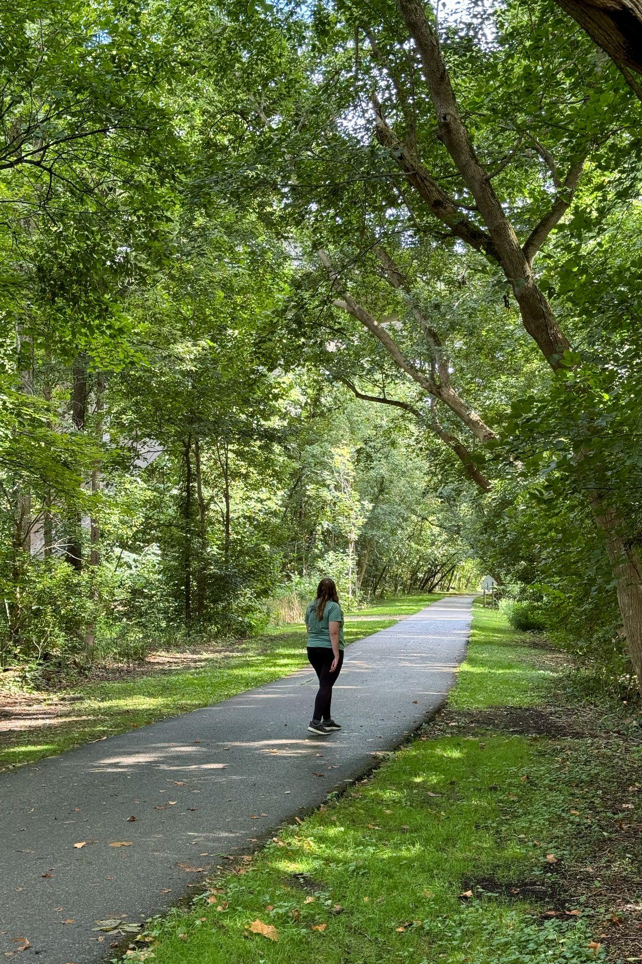 Lydia walking down the paved Loveland Bike Trail, which is surrounded by trees