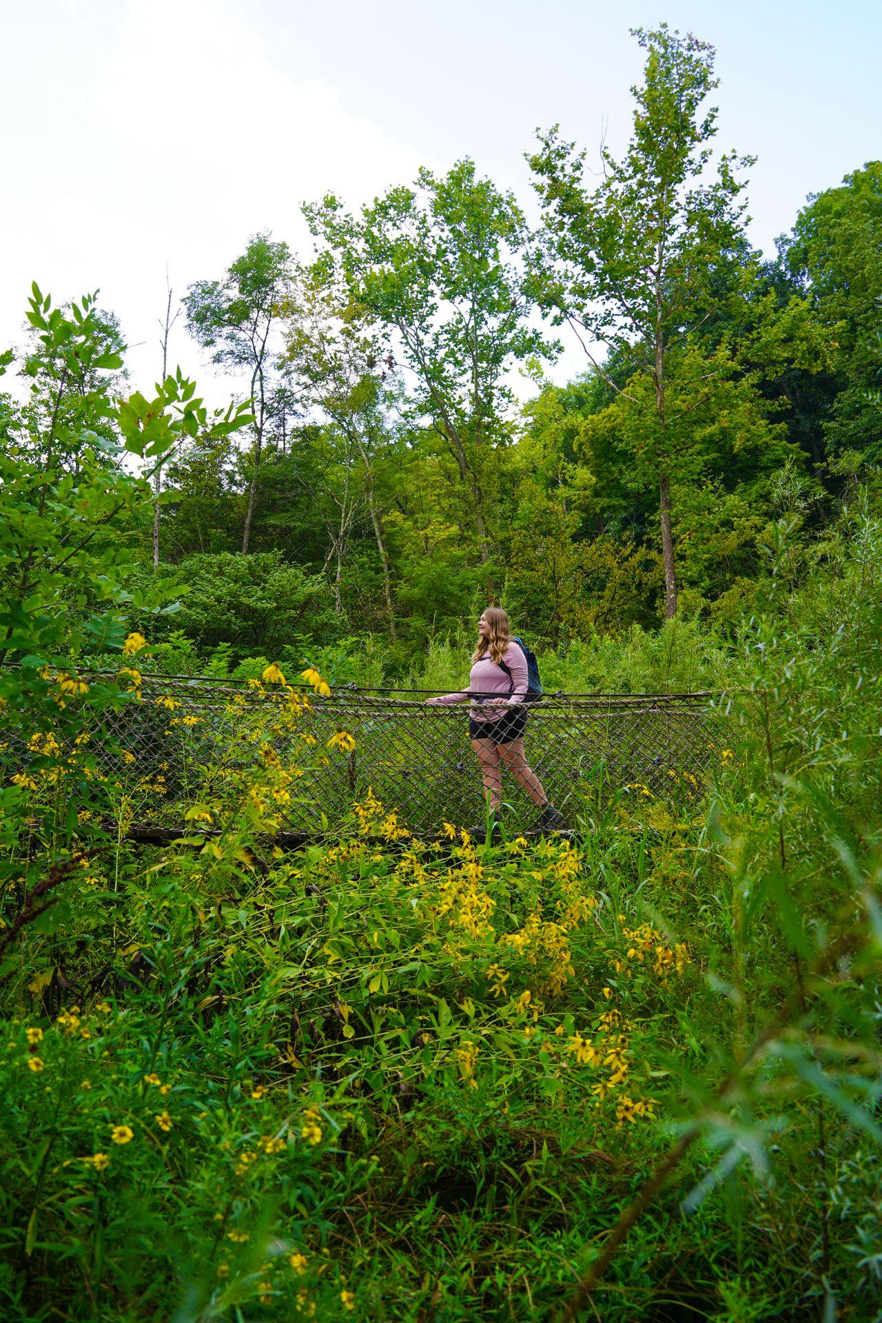 Lydia on a swinging bridge that is surrounded by greenery and yellow flowers