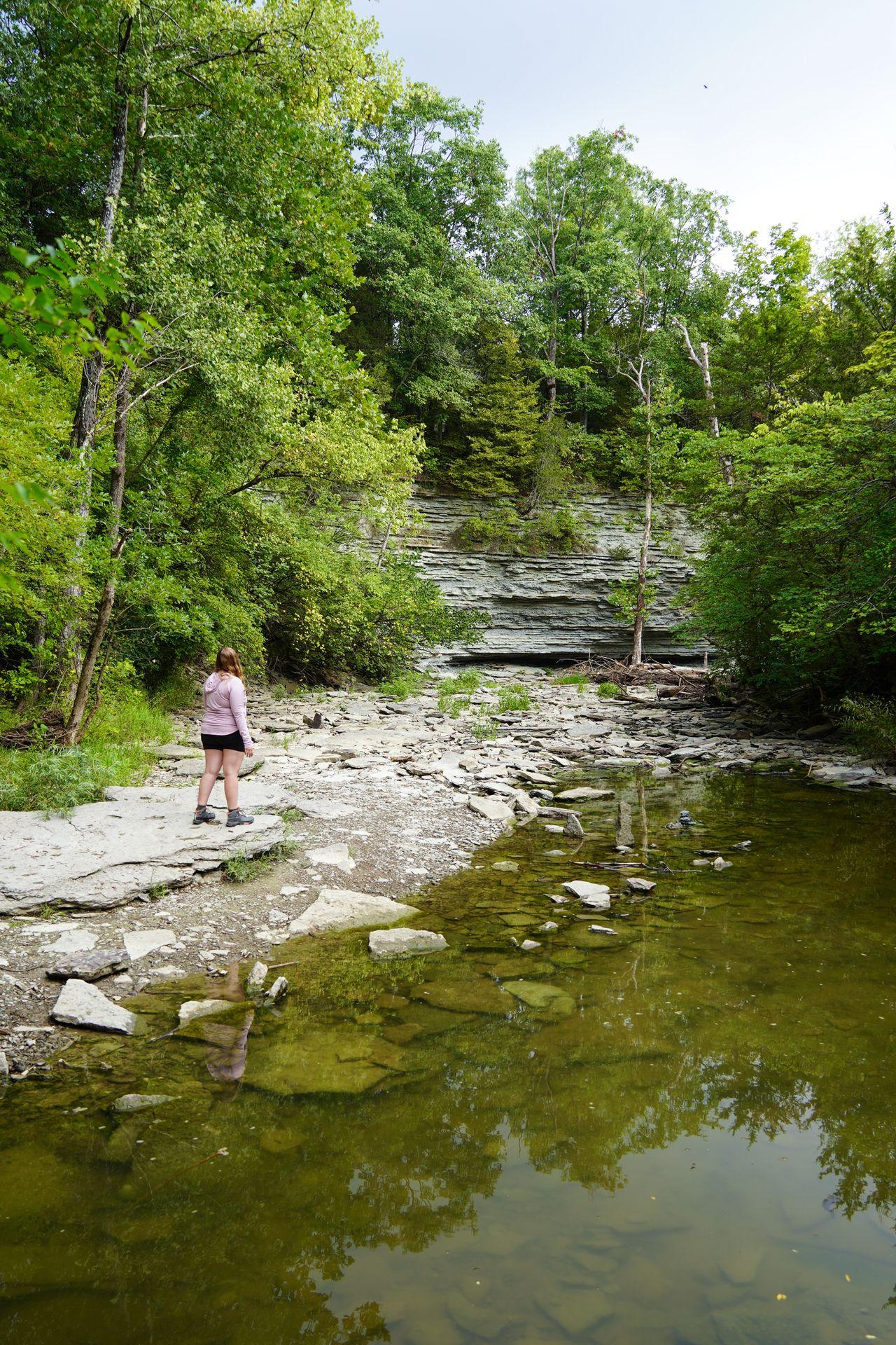 Lydia standing next to a river with limestone rocks in the distance in Caesar Creek State Park