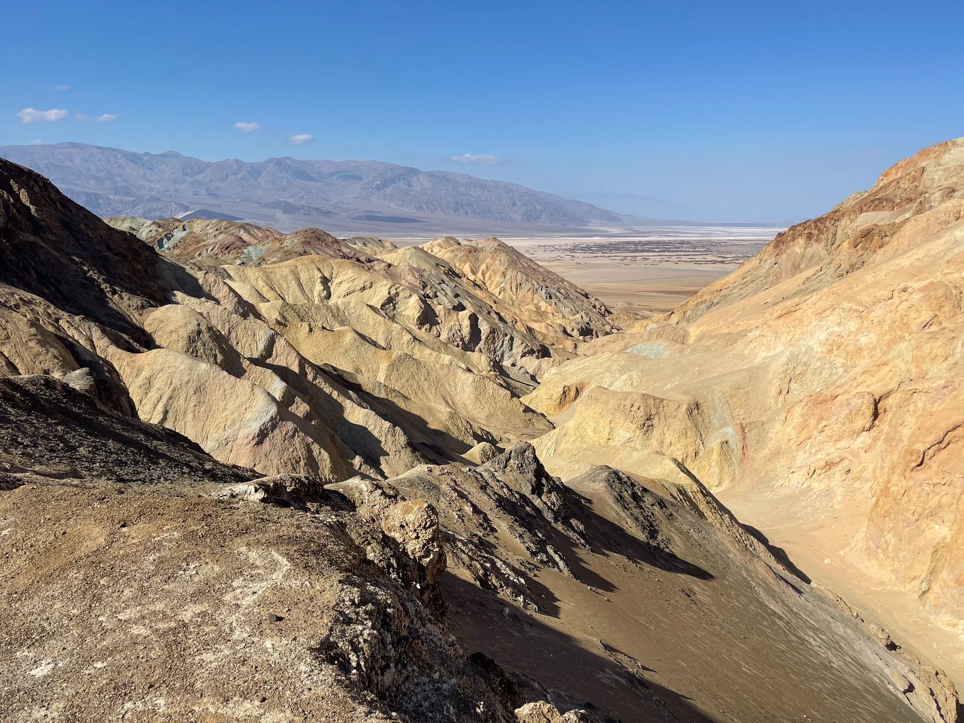 A view of a golden canyon with salt flats and mountains in the distance.